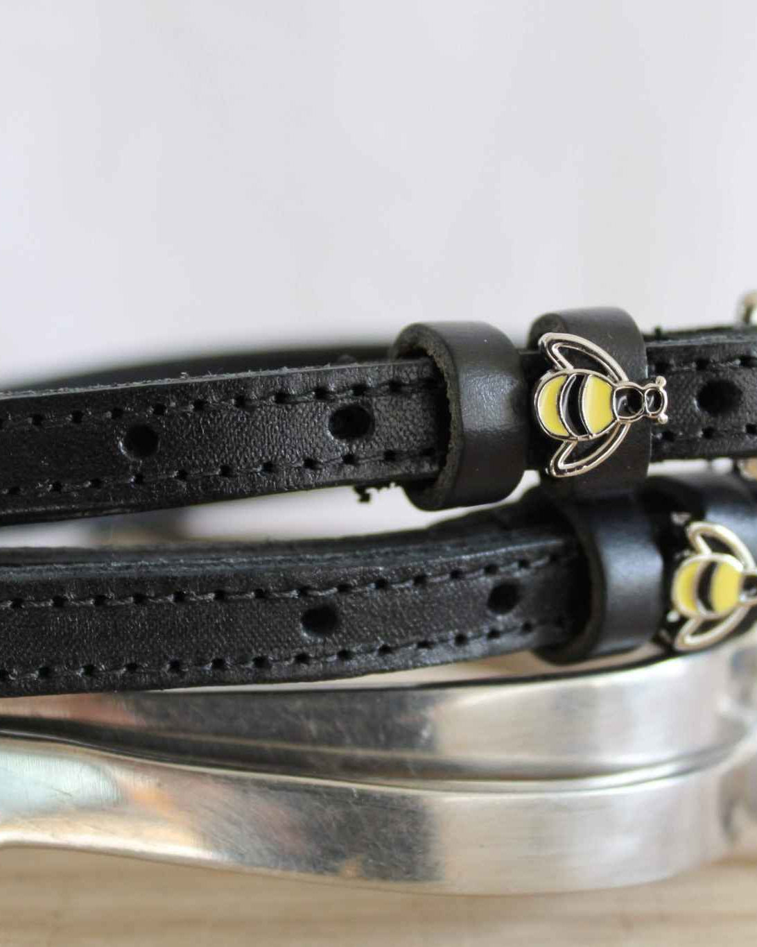 Side view of black bee spur straps resting on a silver spur, showing buckle and charm