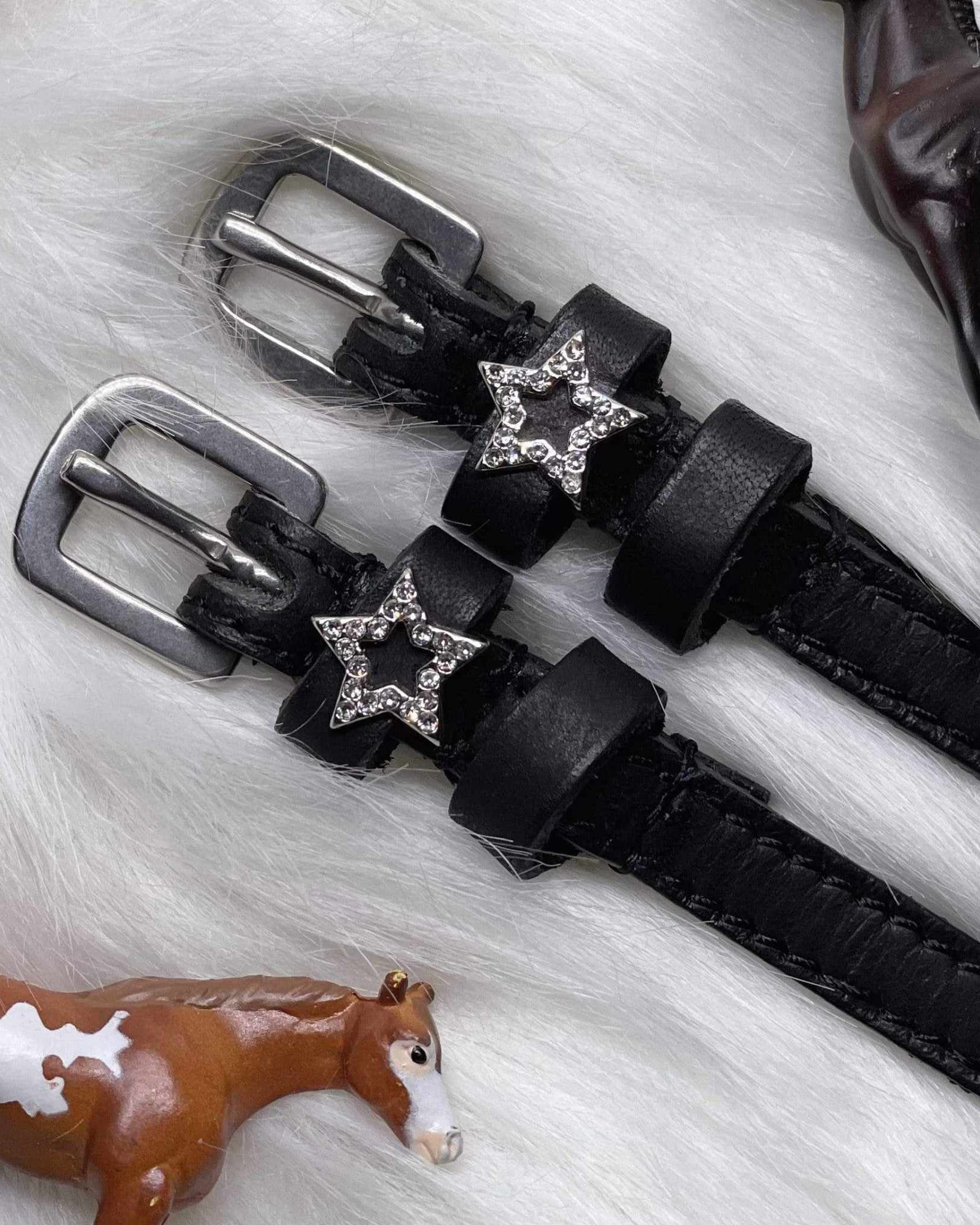 Angled close-up of rhinestone star charms on spur straps over white fur with toy horses