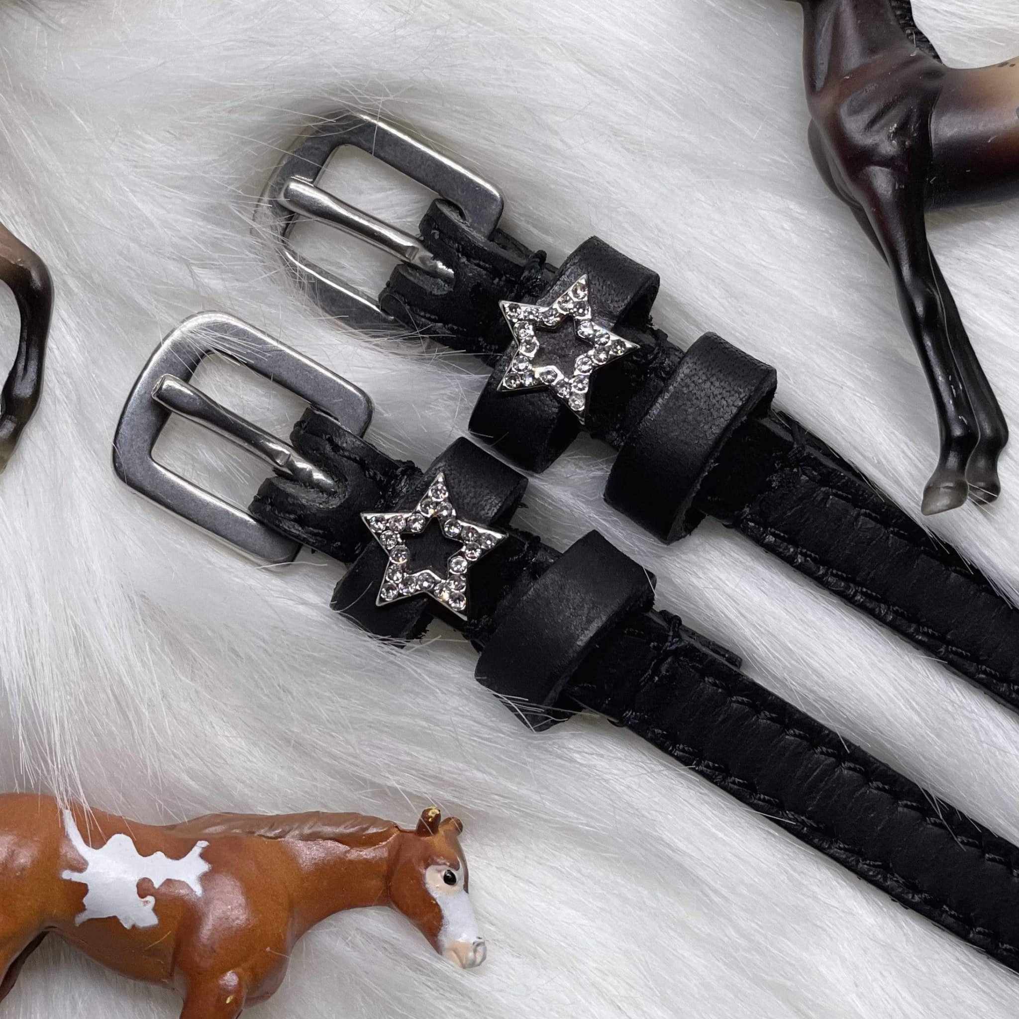 Angled close-up of rhinestone star charms on spur straps over white fur with toy horses