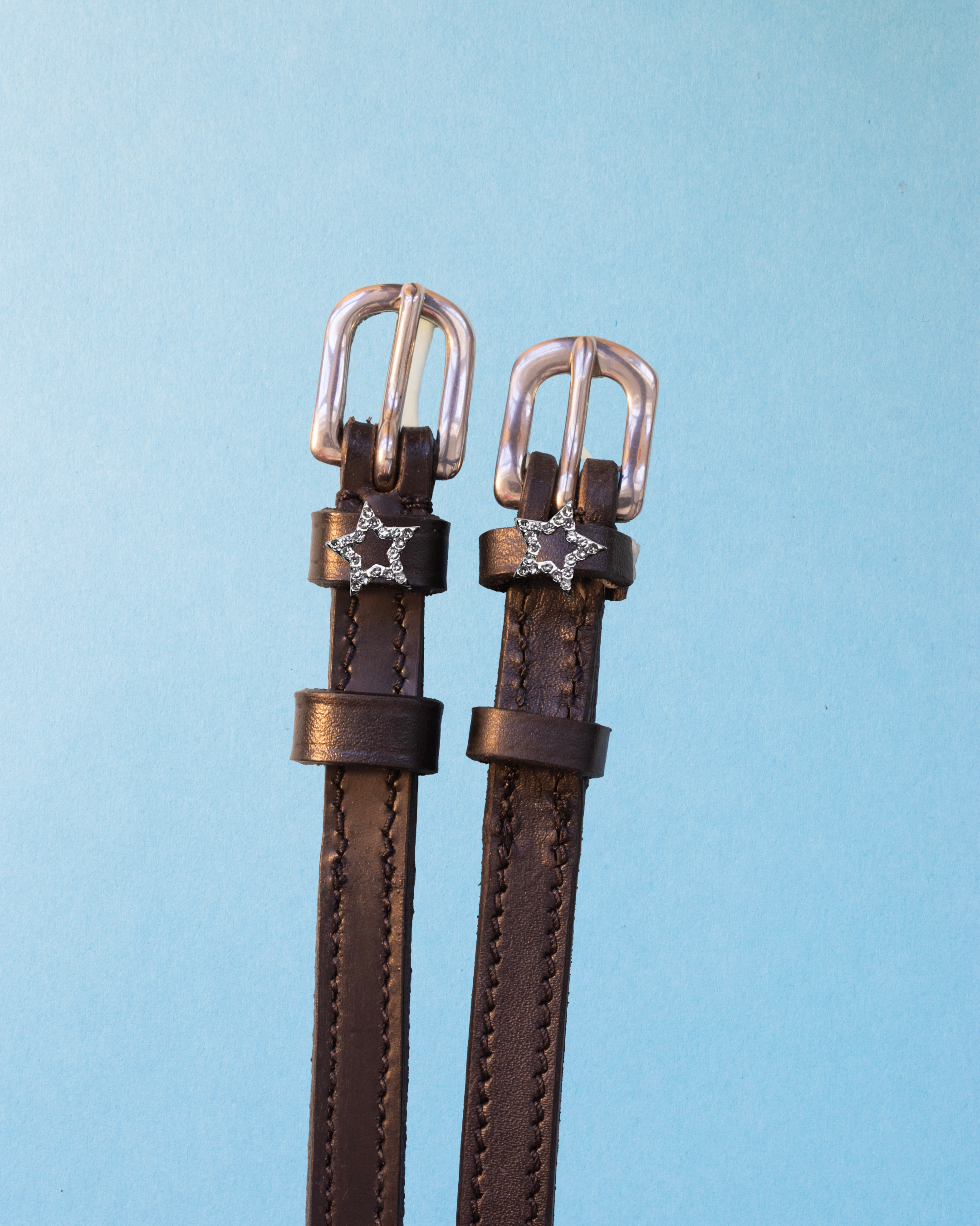 Brown leather crystal star outline spur straps on a light blue background