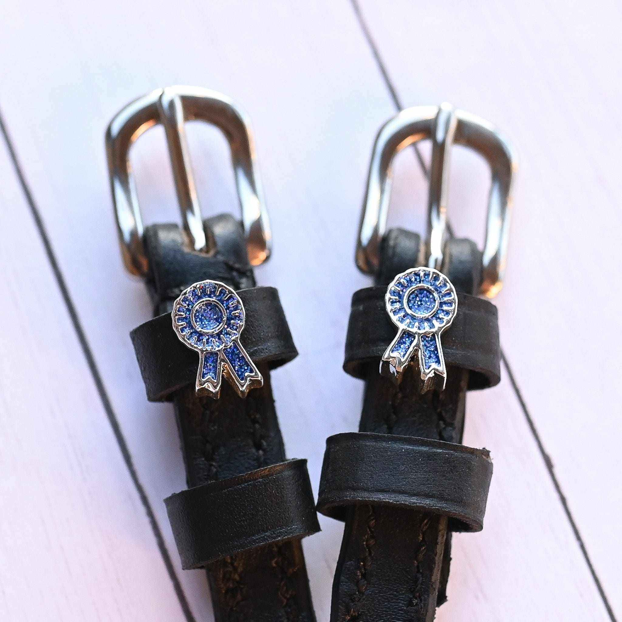 Blue ribbon rosette spur straps with silver buckles on white-painted wood planks