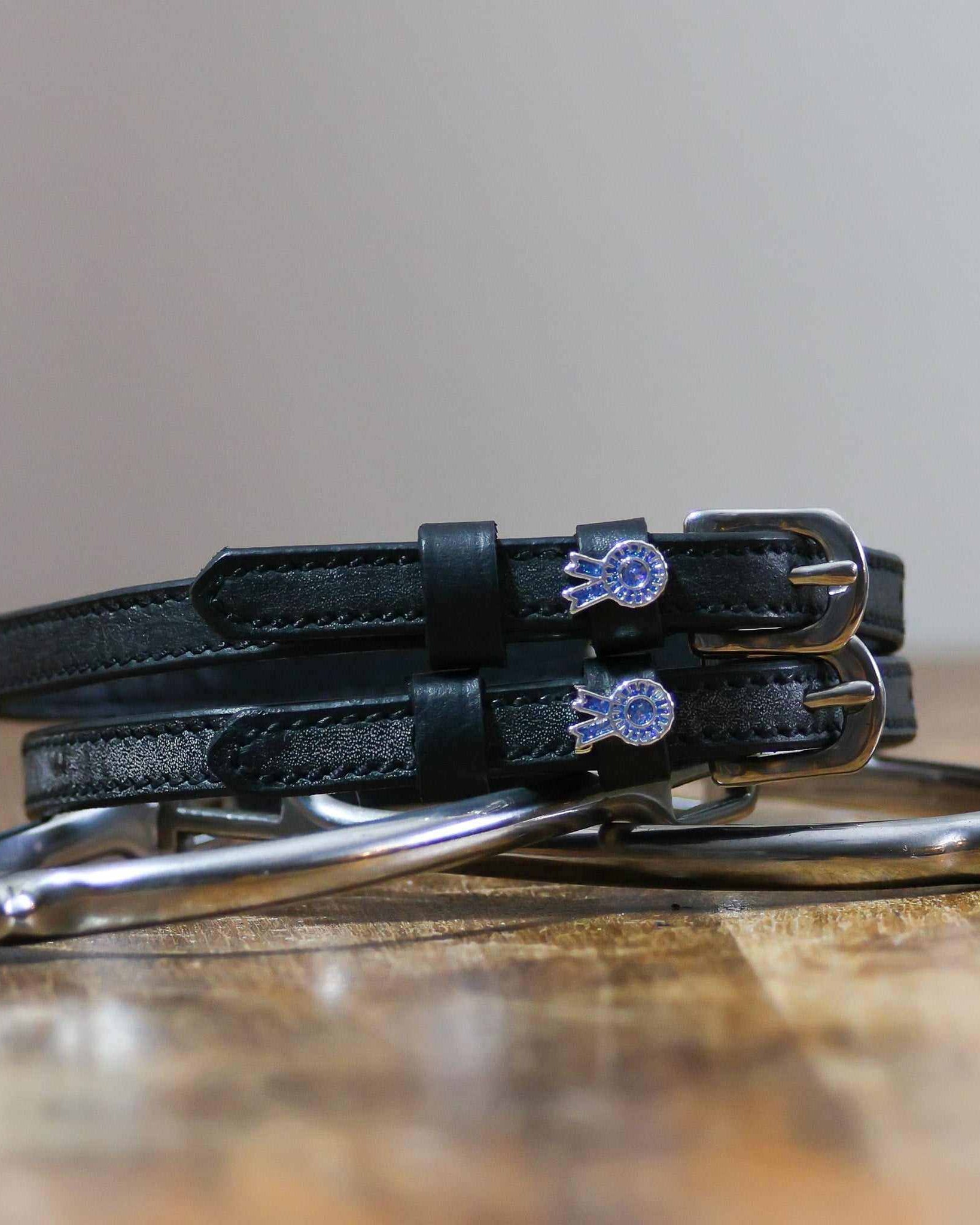 Blue ribbon spur straps coiled on a silver stirrup on a wooden table