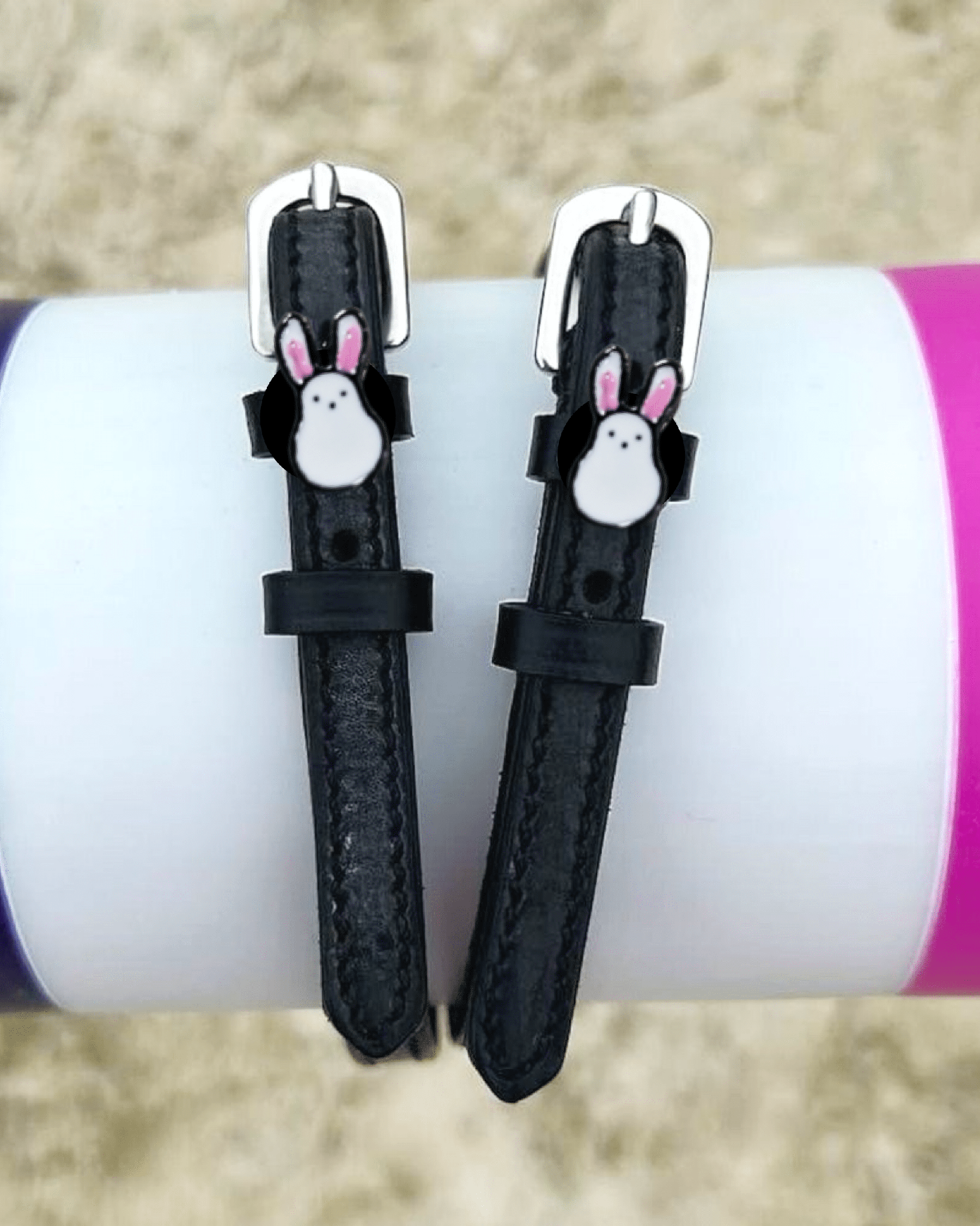 Bunny Hop spur straps wrapped around a tumbler on sand, white ManeJane bunny charm