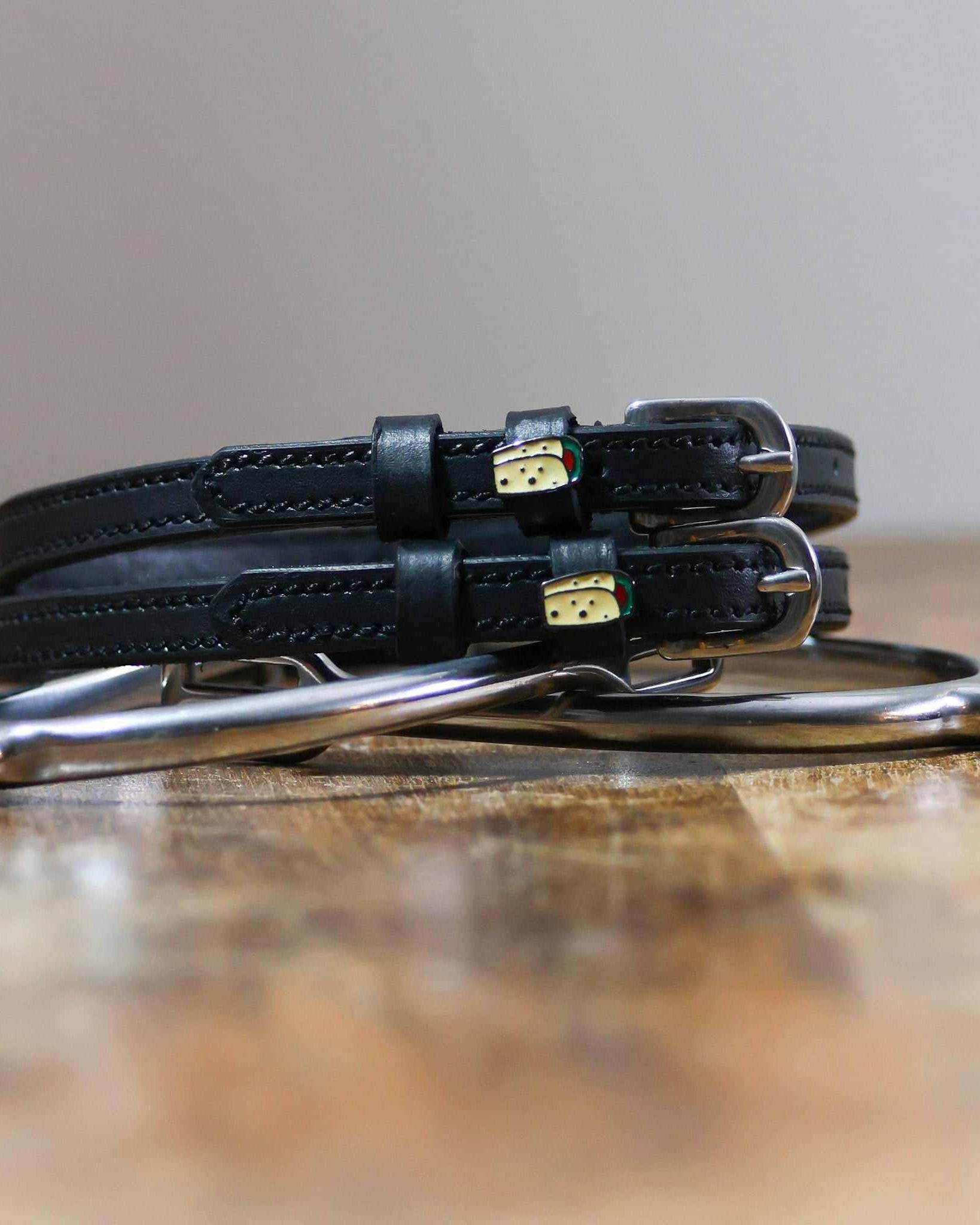Coiled black leather burrito spur straps stacked on a silver spur on a wooden table