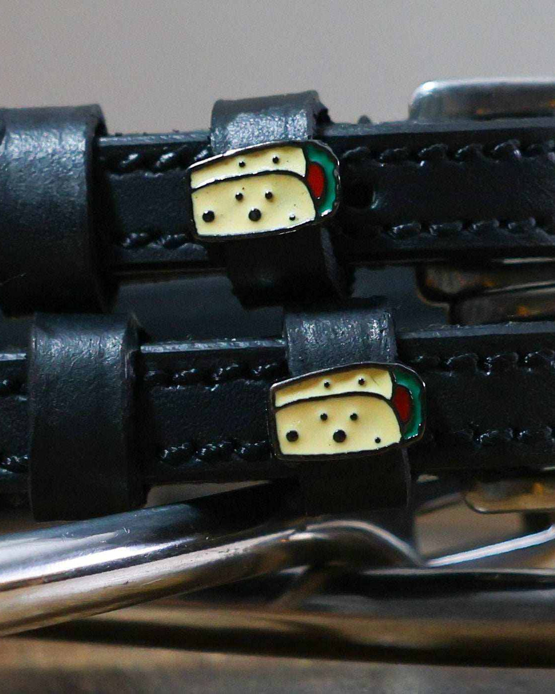 Close-up of enamel burrito charms on the keepers of black leather ManeJane spur straps