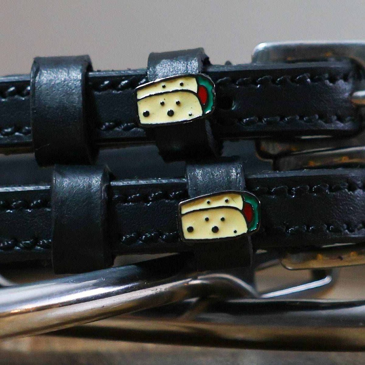 Close-up of enamel burrito charms on the keepers of black leather ManeJane spur straps