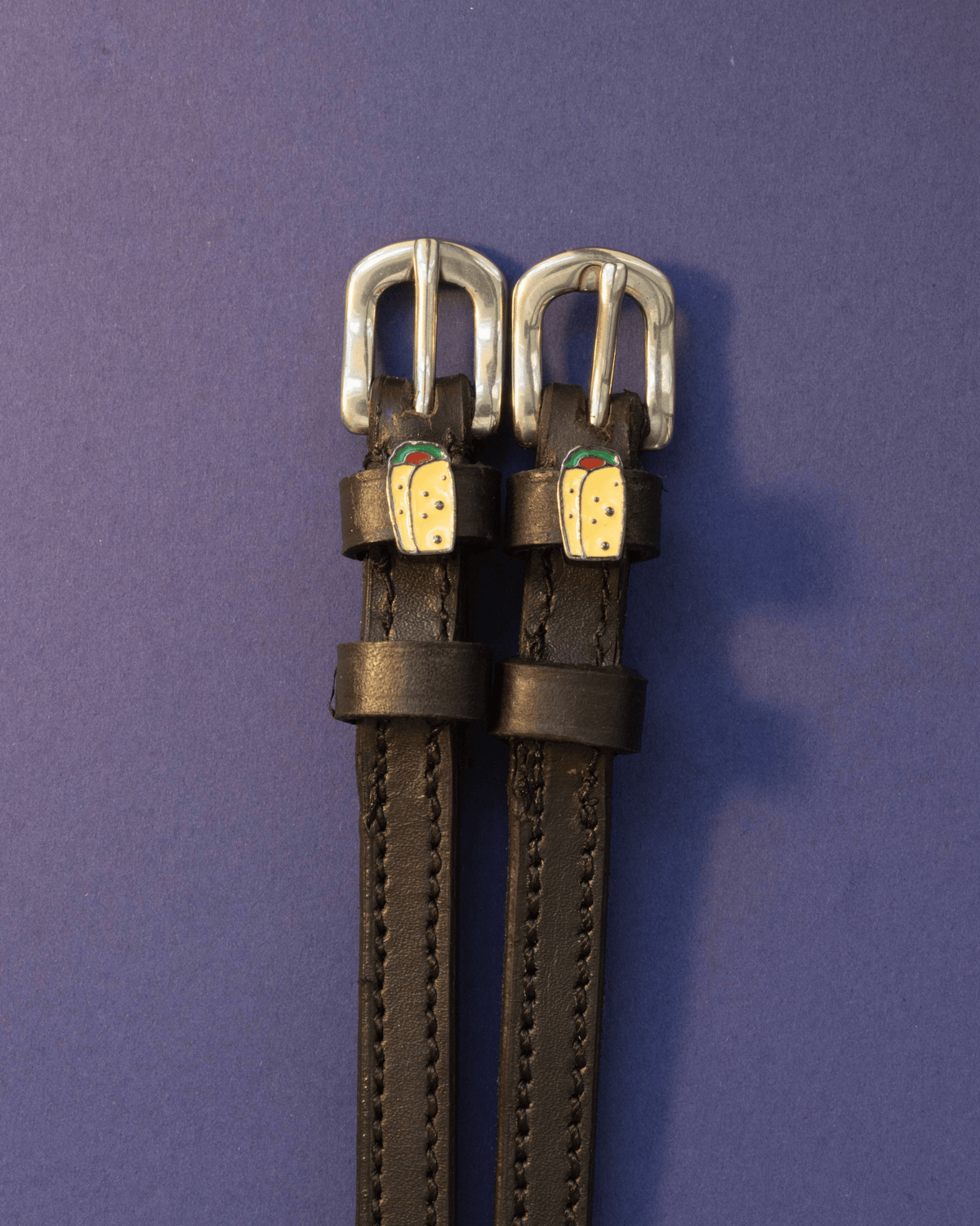Black leather ManeJane burrito spur straps with silver buckles on a deep purple background