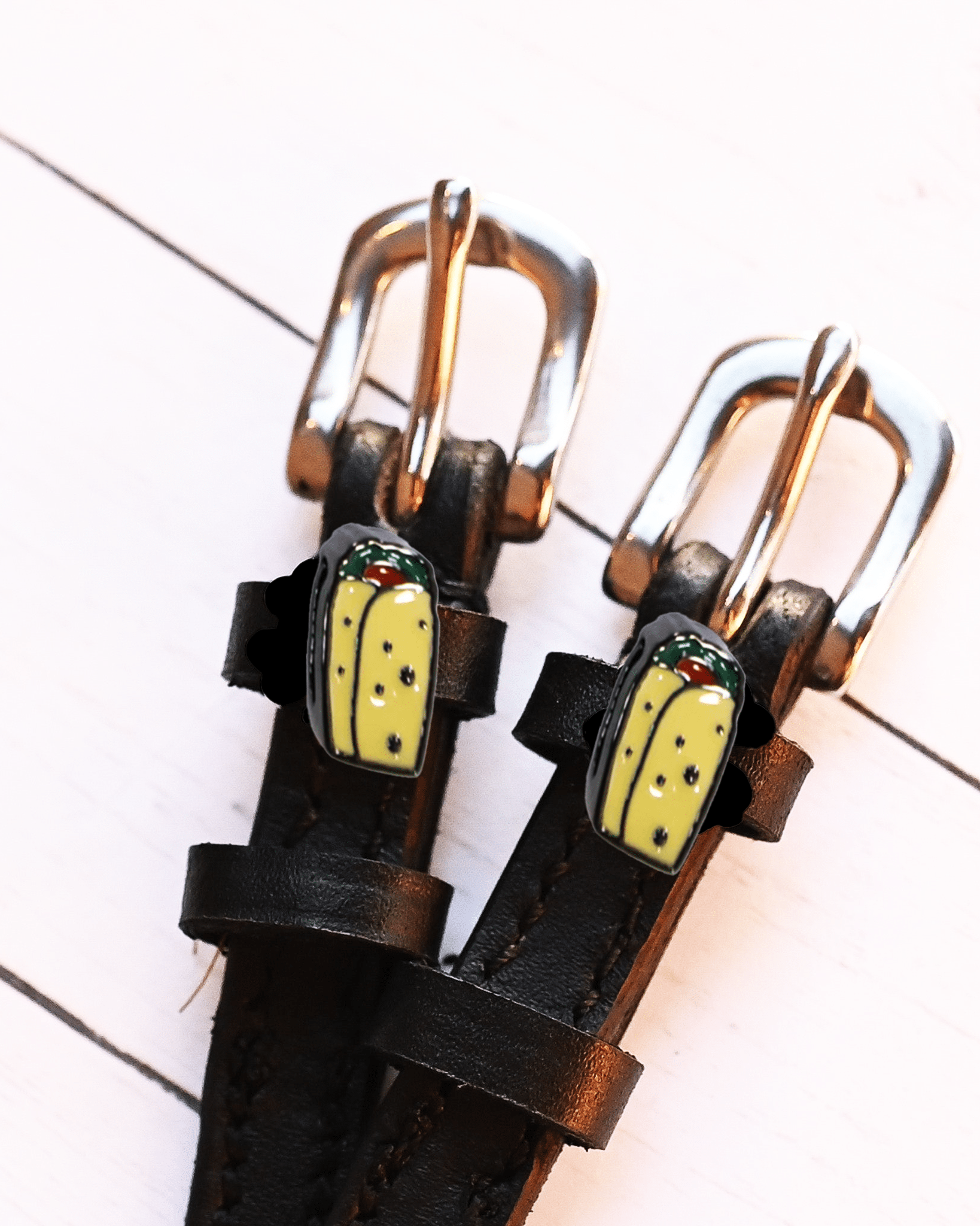 Overhead of black leather spur straps with silver buckles and burrito charms on white wood