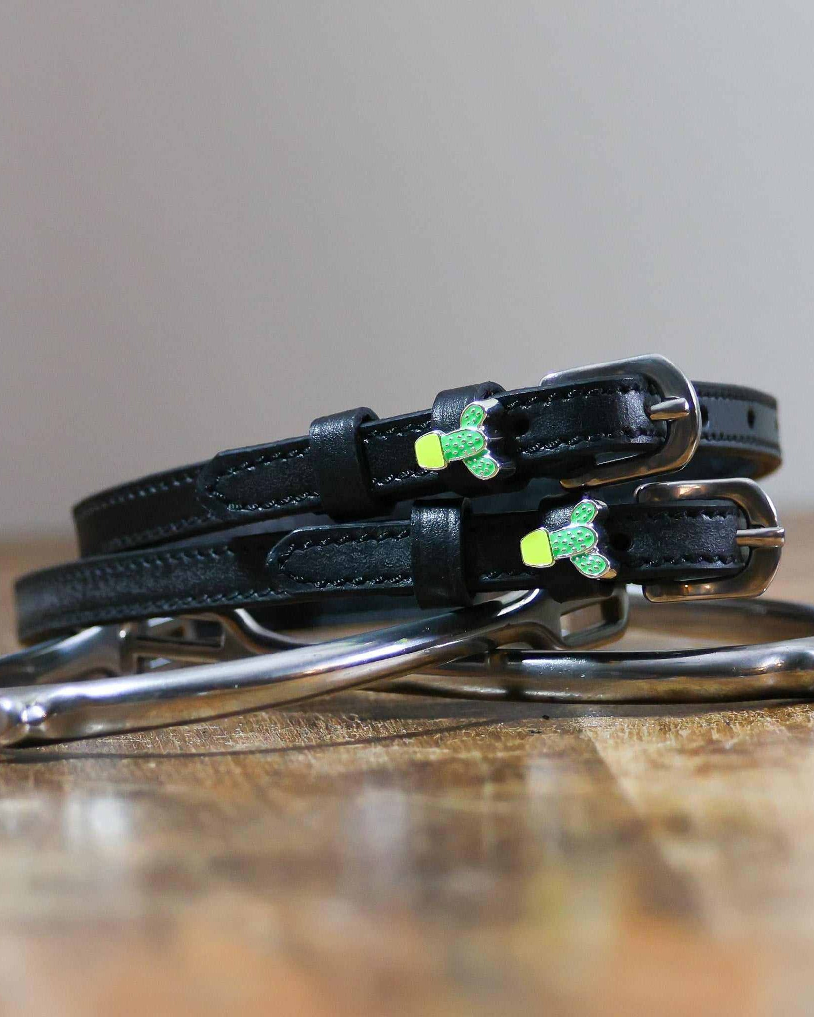 Cactus charm spur straps coiled beside a stirrup on a wooden tabletop