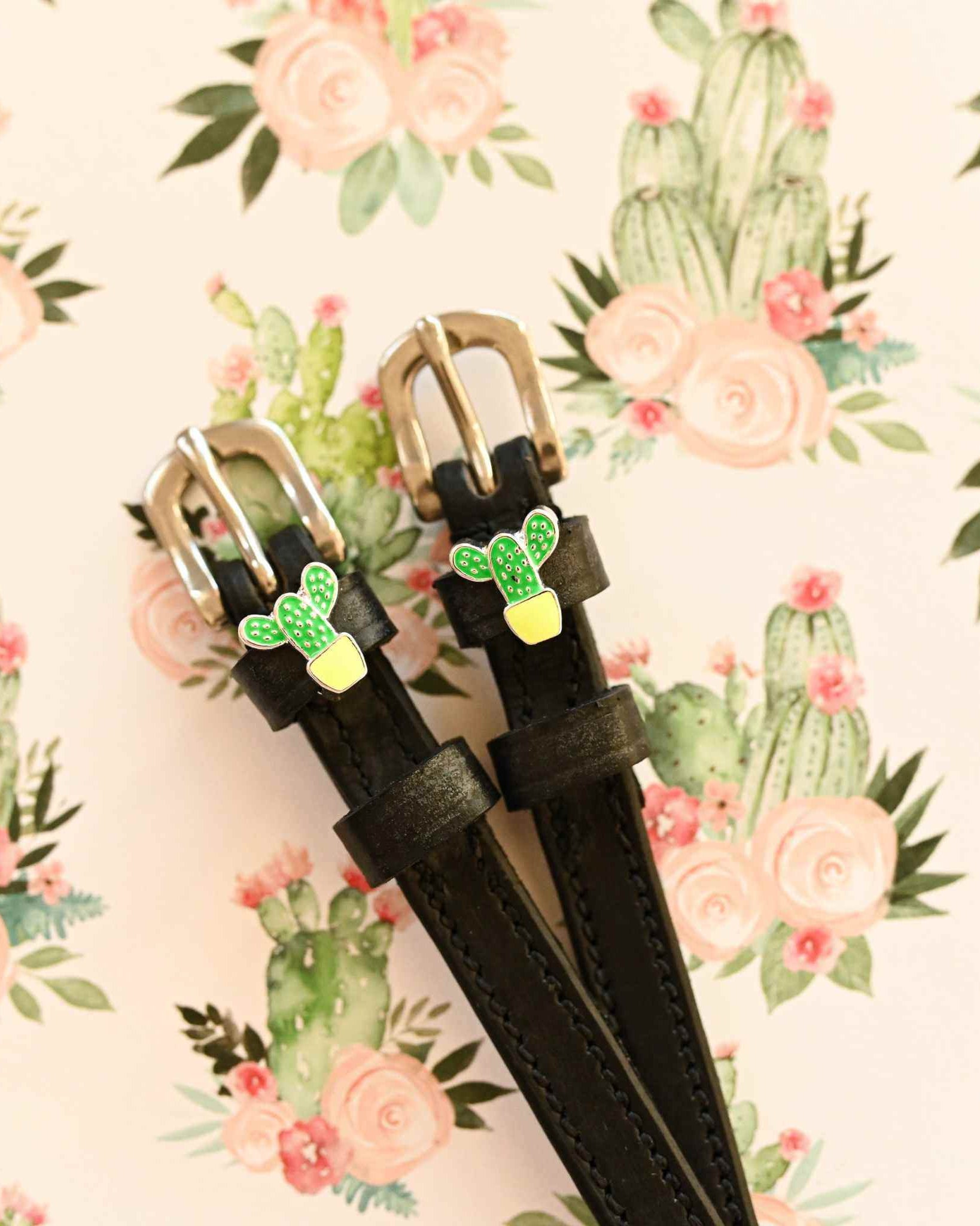 Pair of cactus charm spur straps laid on a floral cactus print background