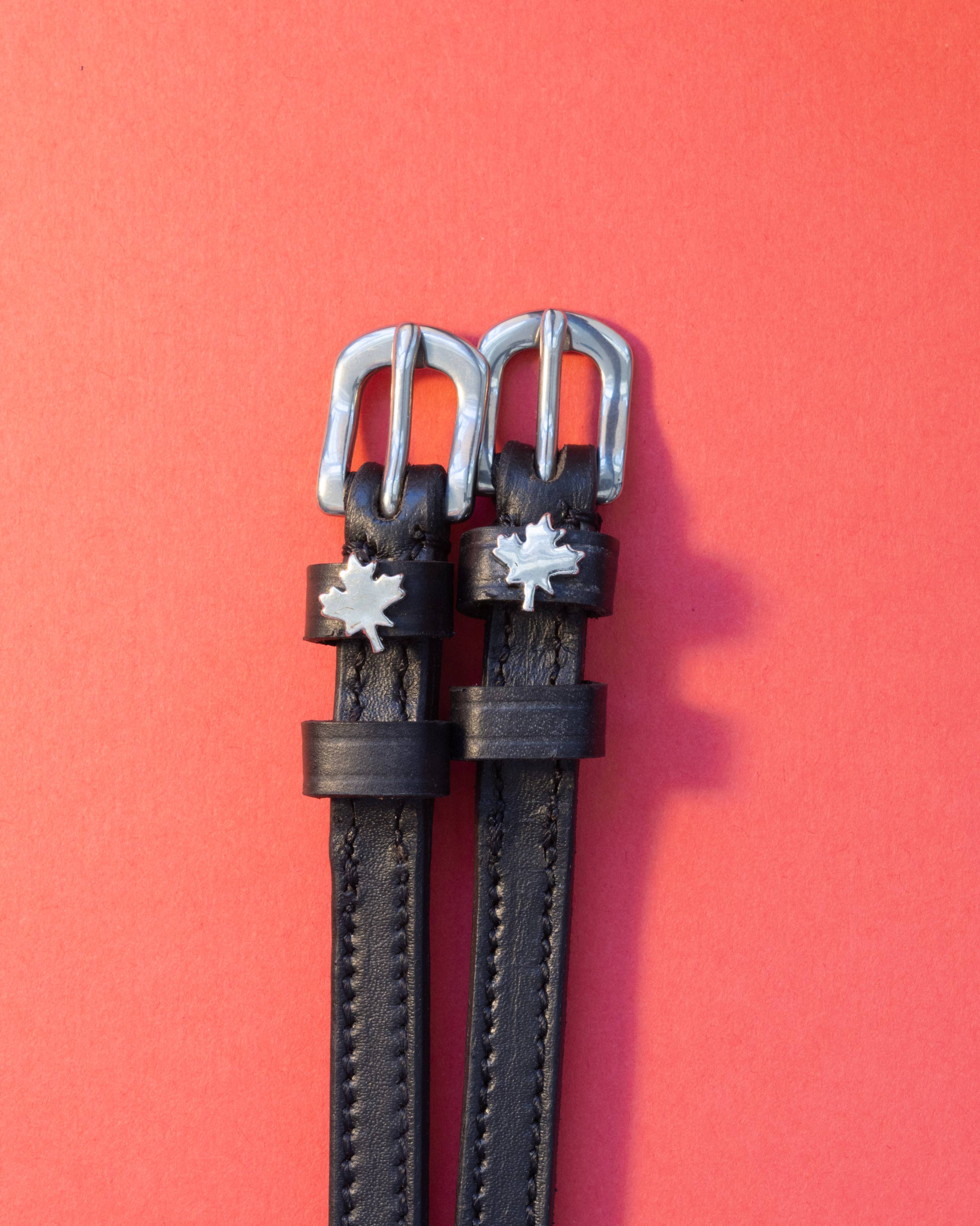 Black leather maple leaf spur straps with silver buckles on a coral red background