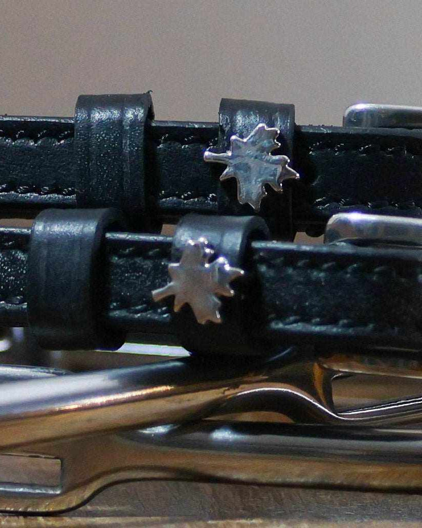 Close-up of silver maple leaf charms on black leather ManeJane spur straps over spur hardware
