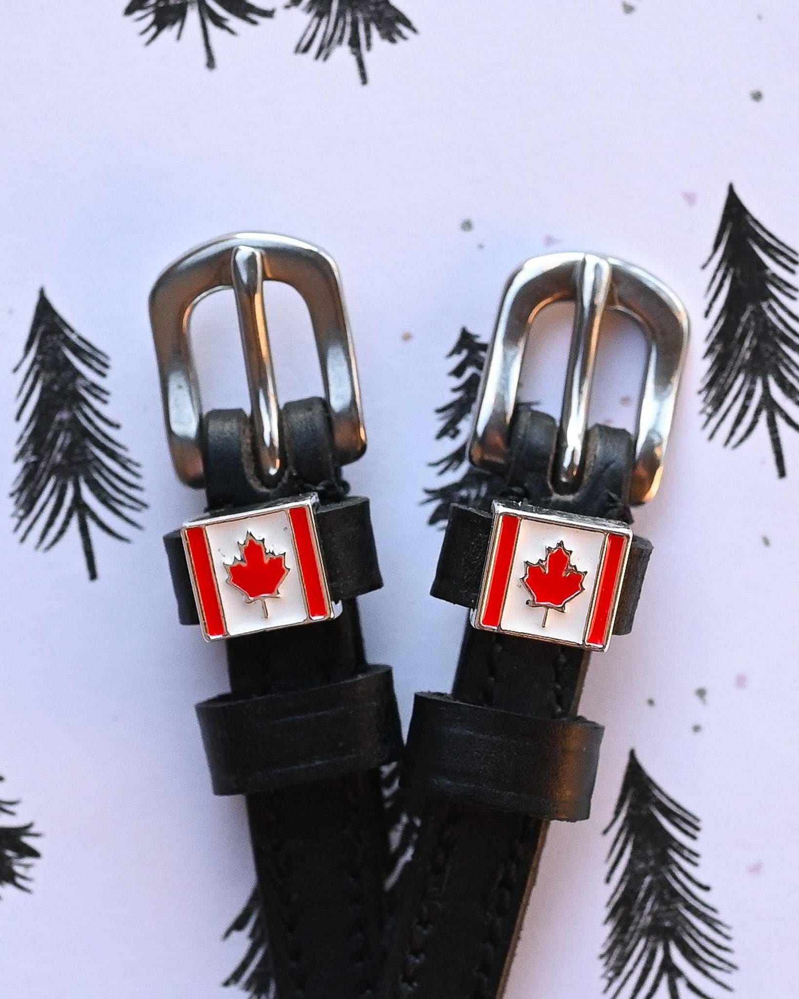 Canadian flag spur straps with silver buckles on a lilac pine-tree print background