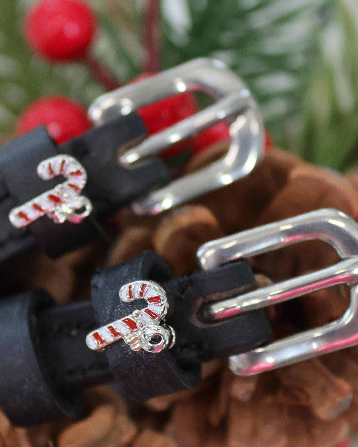 Close-up of candy cane charms on black spur straps among pinecones and holly berries