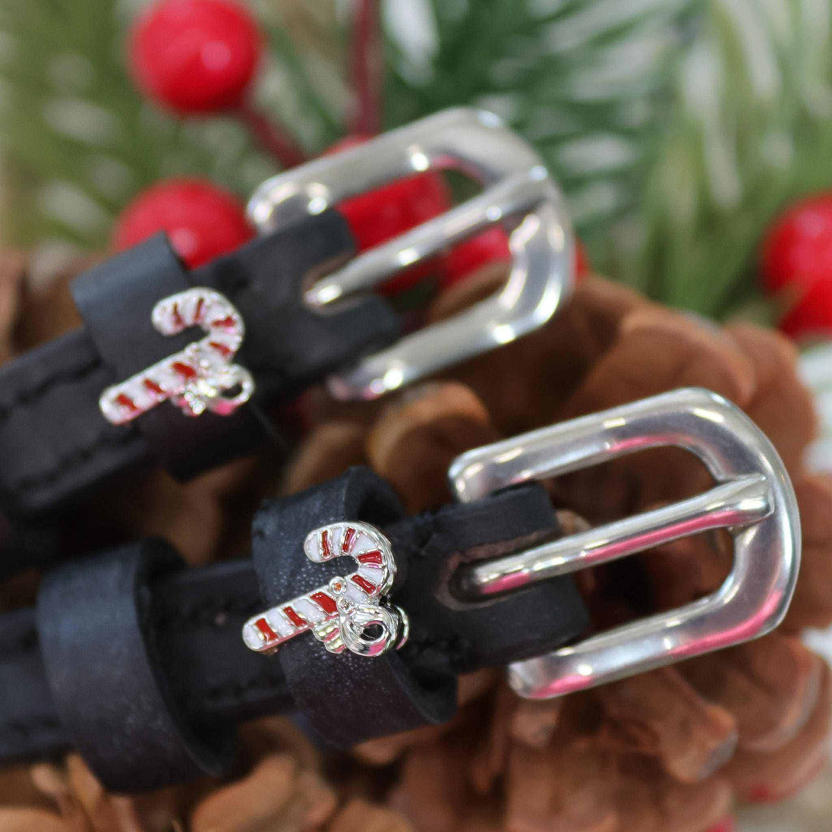 Close-up of candy cane charms on black spur straps among pinecones and holly berries