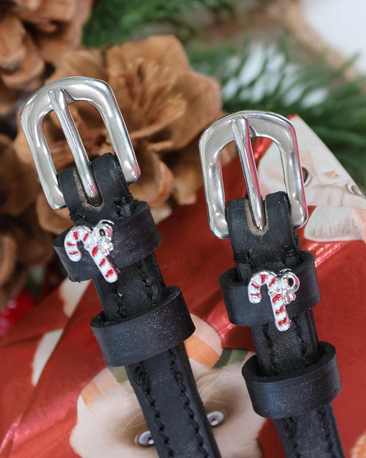 Silver buckles and candy cane charms of spur straps on a festive pinecone setting