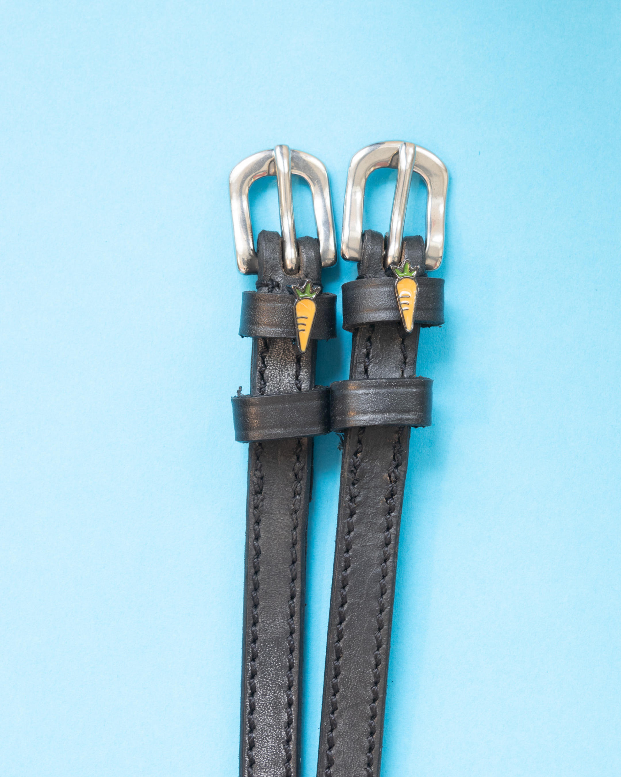 Black leather carrot spur straps with silver buckles flat-laid on a light blue background