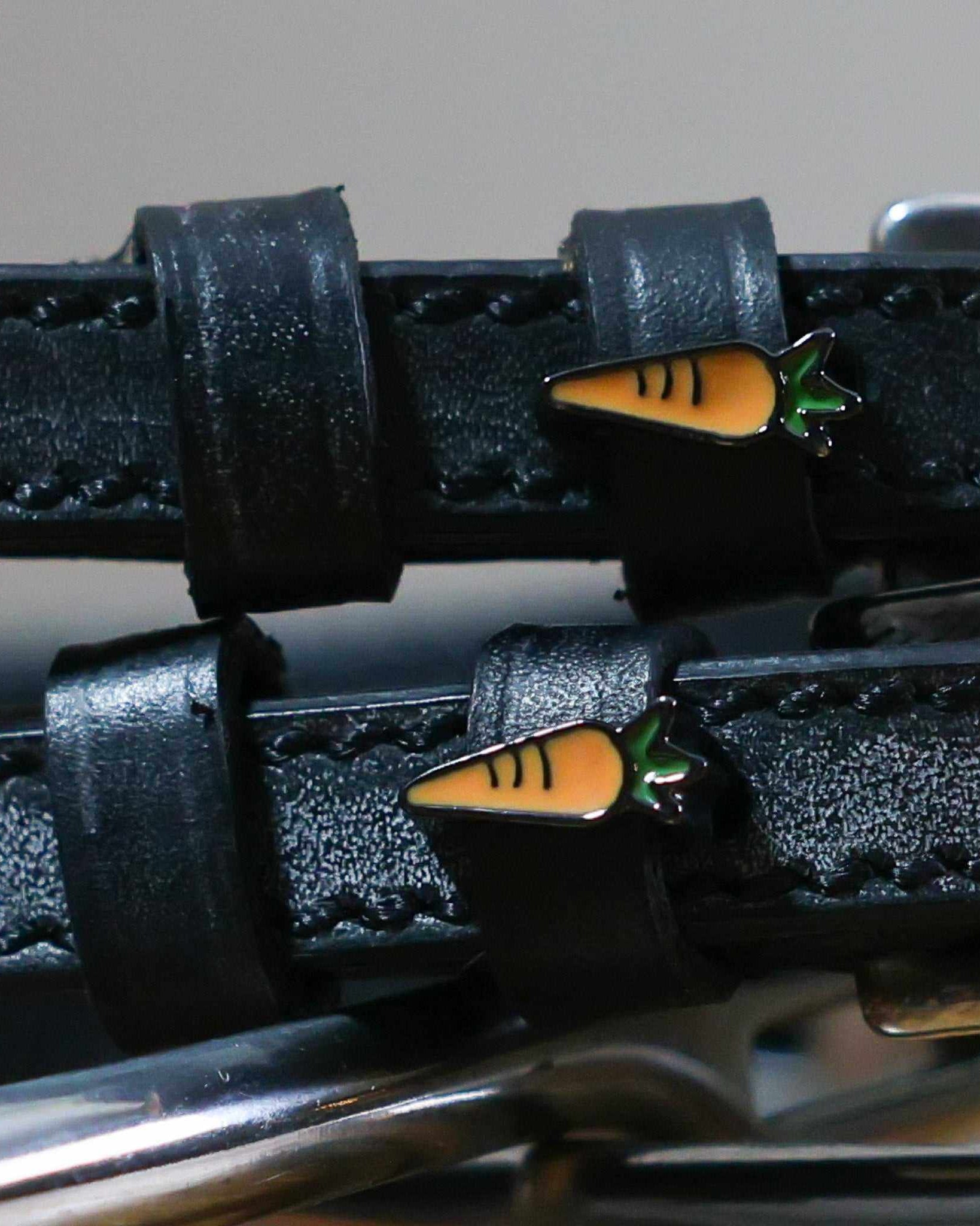Close-up of orange carrot charms on the keepers of black leather ManeJane spur straps