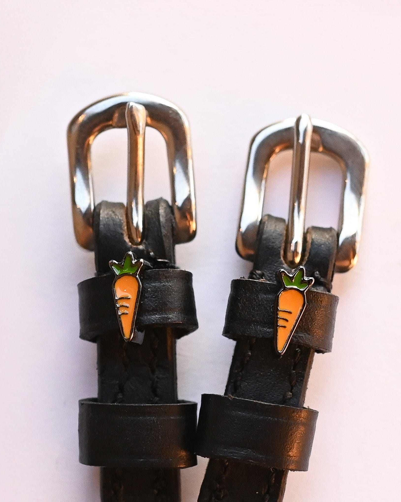 Silver buckles and carrot charms on black leather spur straps, close-up on a pink background