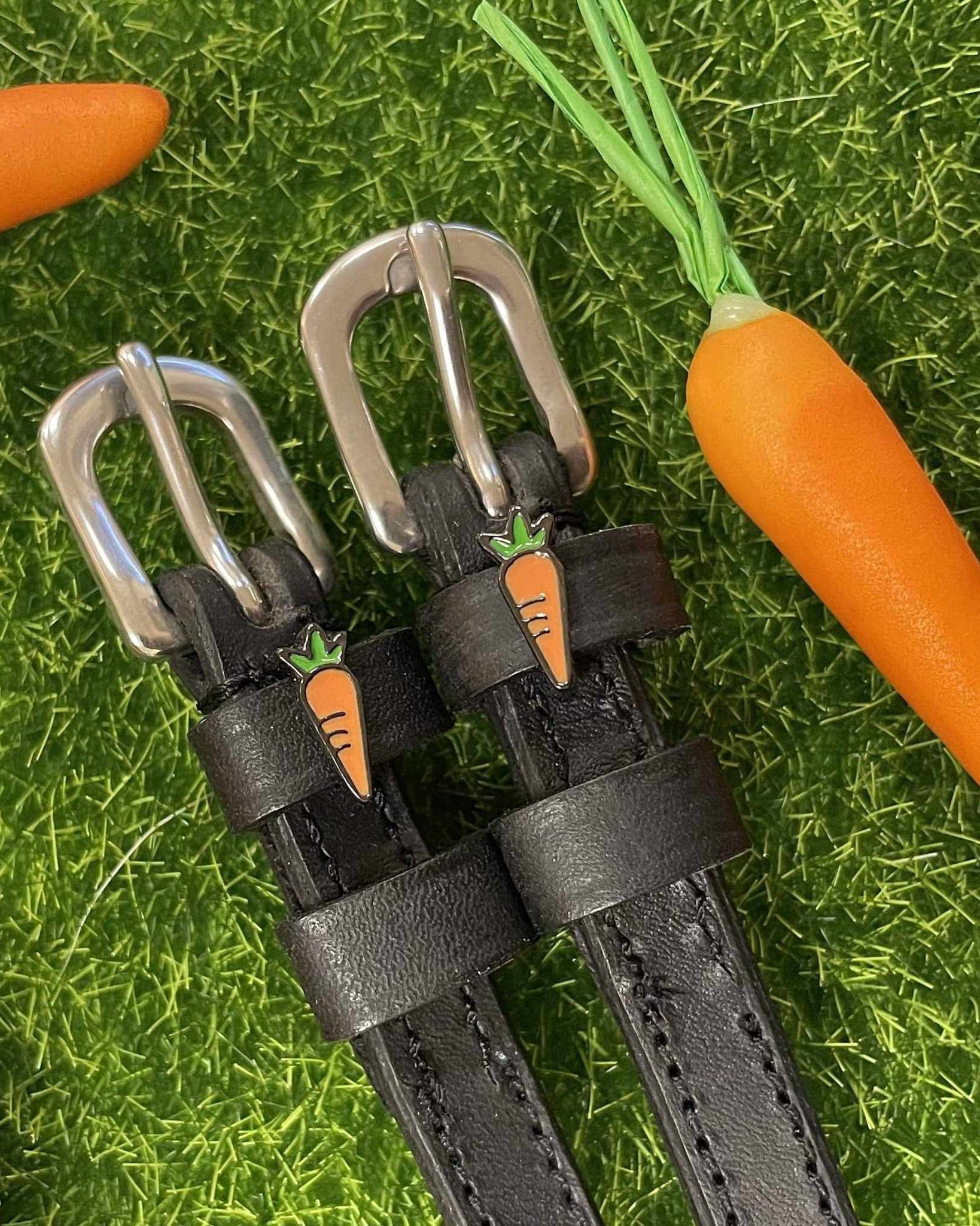 Black leather carrot spur straps styled on grass beside real and toy carrots by ManeJane