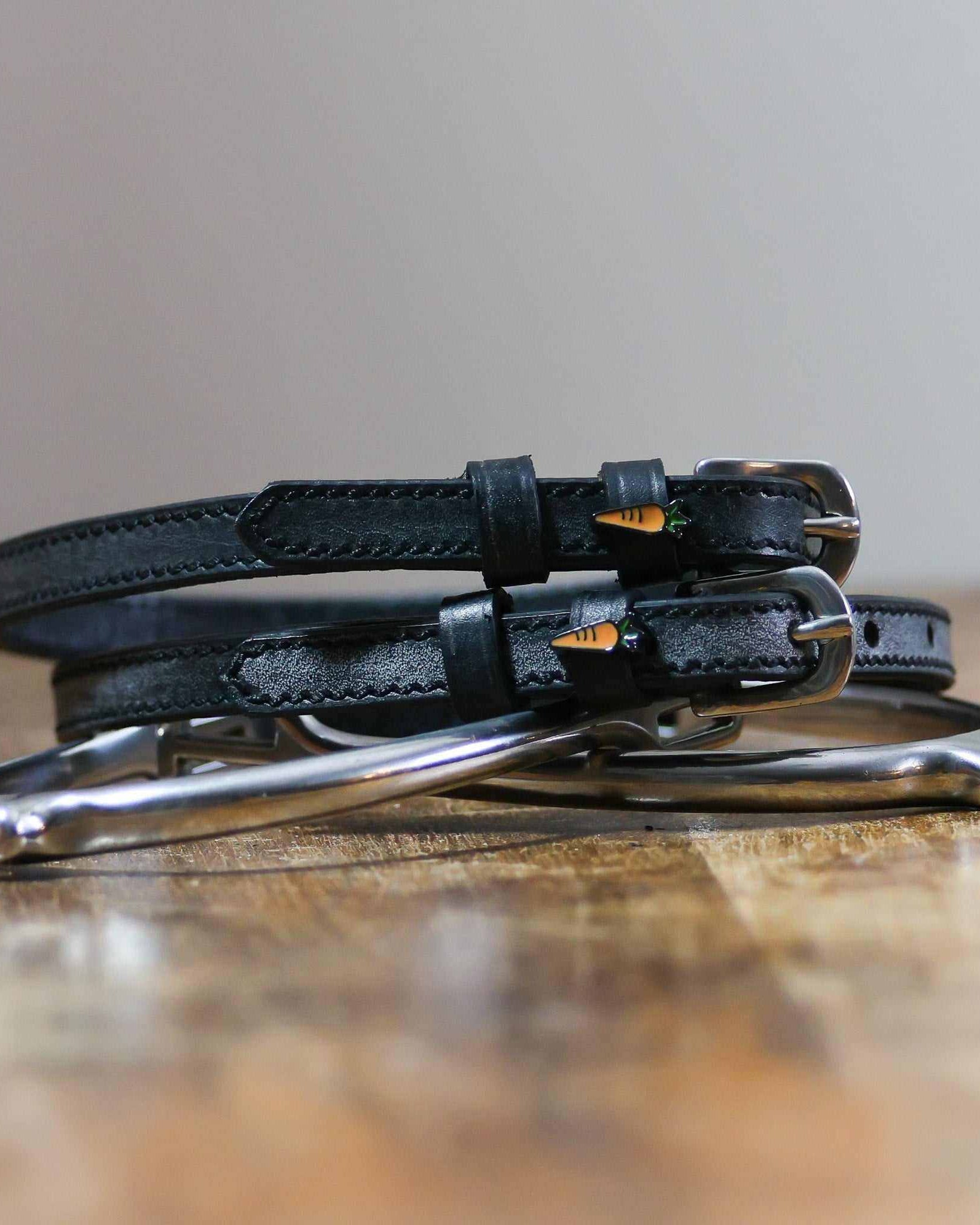 Coiled black leather ManeJane carrot spur straps stacked on a spur on a wooden table