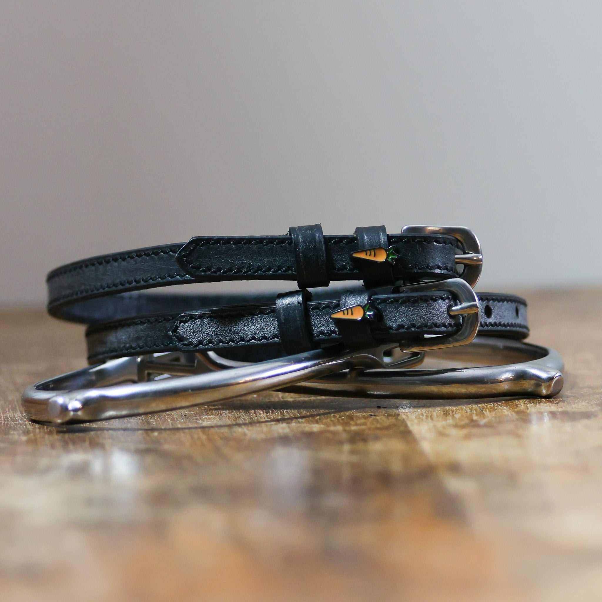 Coiled black leather ManeJane carrot spur straps stacked on a spur on a wooden table