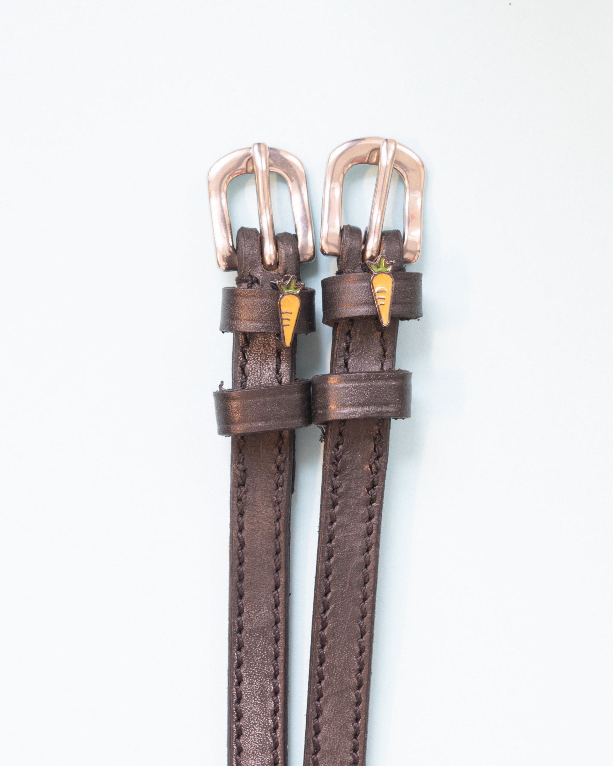 Brown leather spur straps with rose gold buckles and carrot charms on white by ManeJane