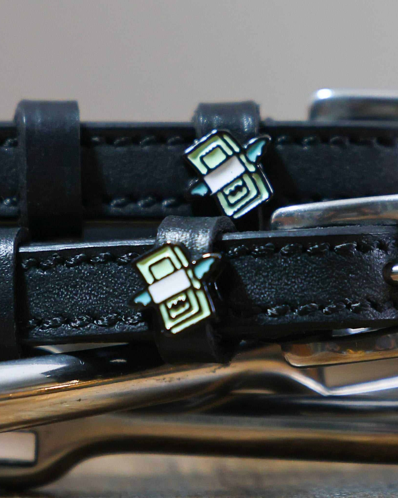 Close-up of a winged stack-of-cash charm on a black leather spur strap