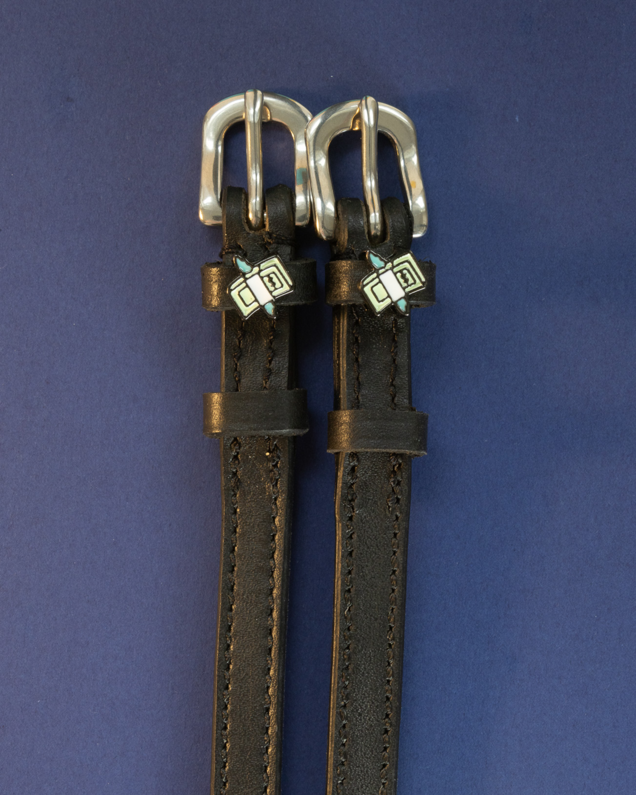 Black leather cash money spur straps flat-laid on a navy background