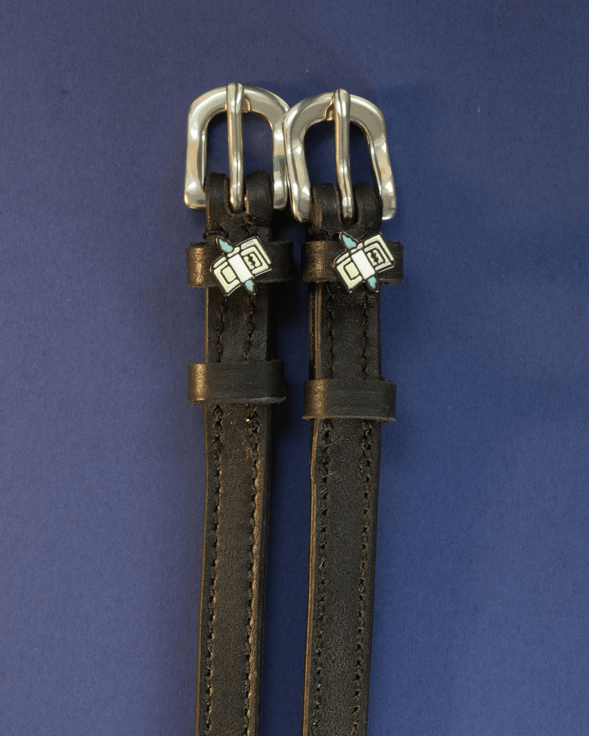 Black leather cash money spur straps flat-laid on a navy background