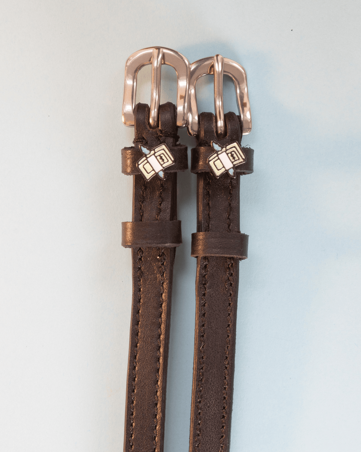 Dark brown leather cash money spur straps with rose-gold buckles on grey