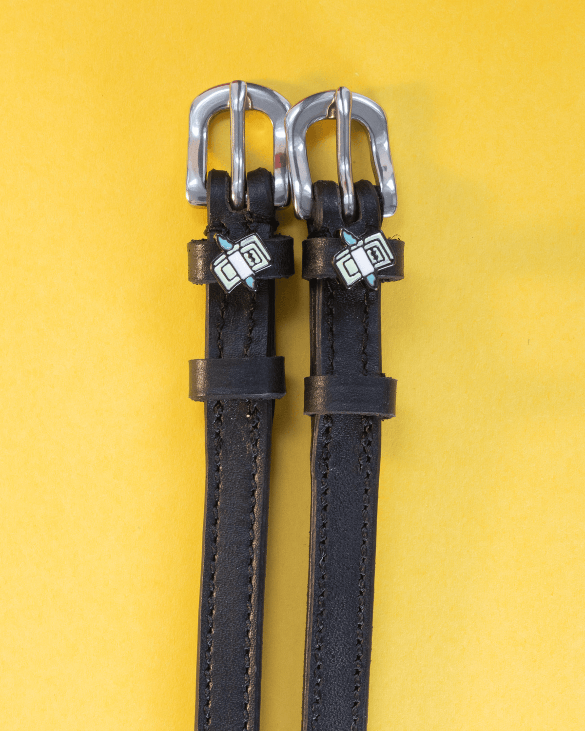 Black leather cash money spur straps flat-laid on a yellow background