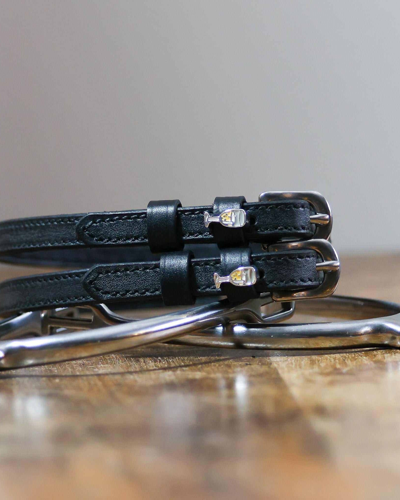 Black leather champagne spur straps coiled on wood beside a metal stirrup