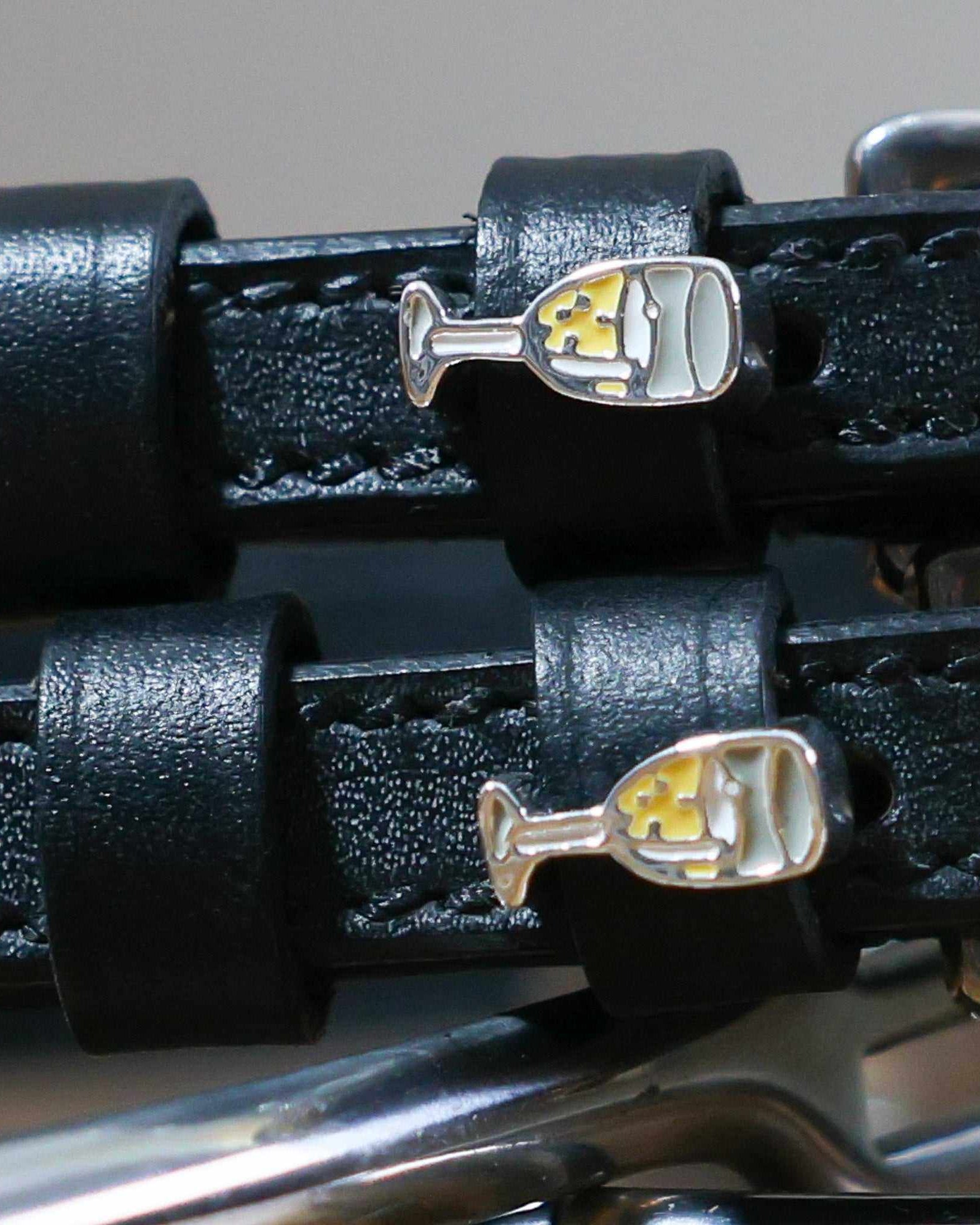 Close-up of enamel champagne-flute charms on black leather spur strap keepers