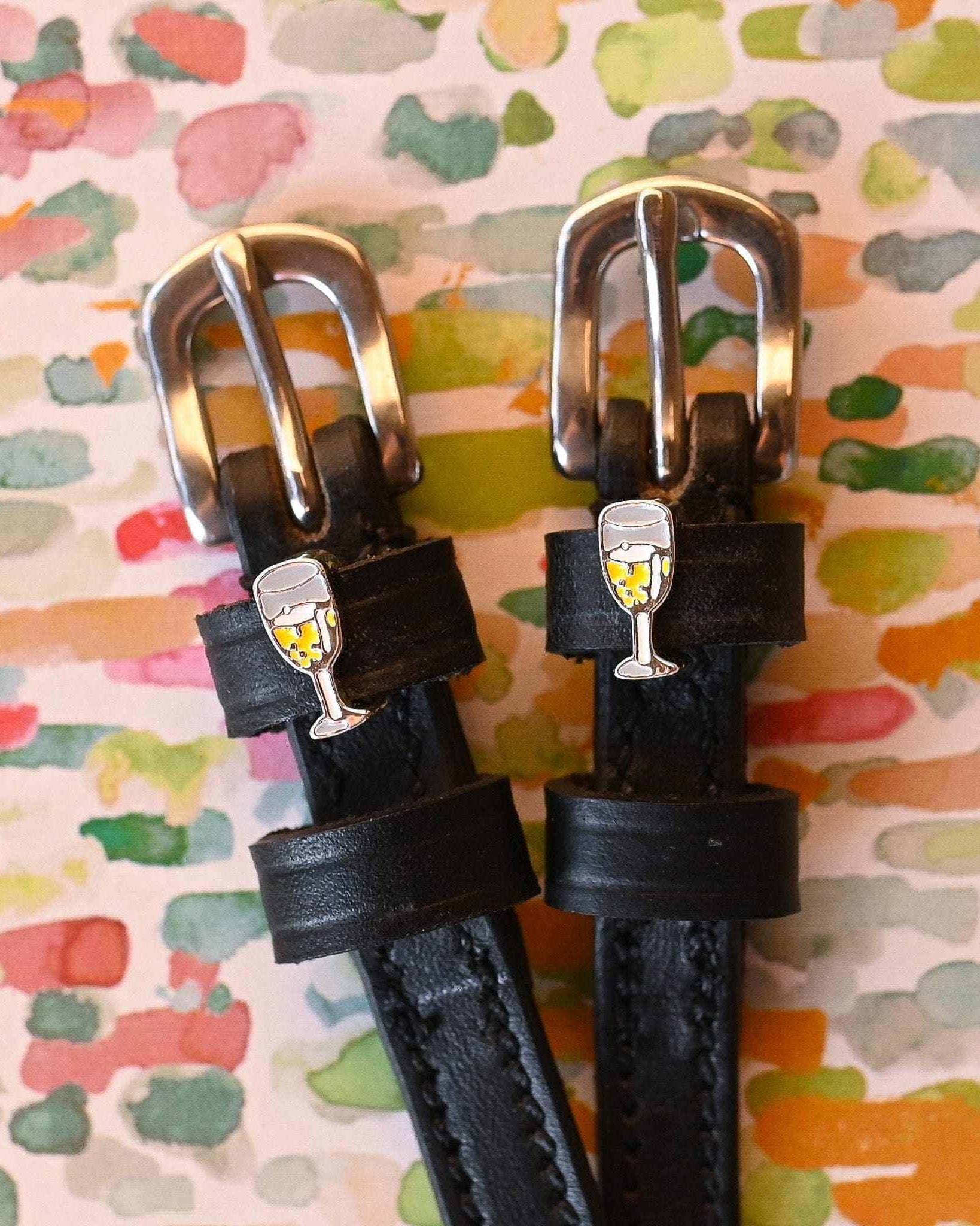Champagne-charm spur straps on a watercolor confetti backdrop, buckle close-up