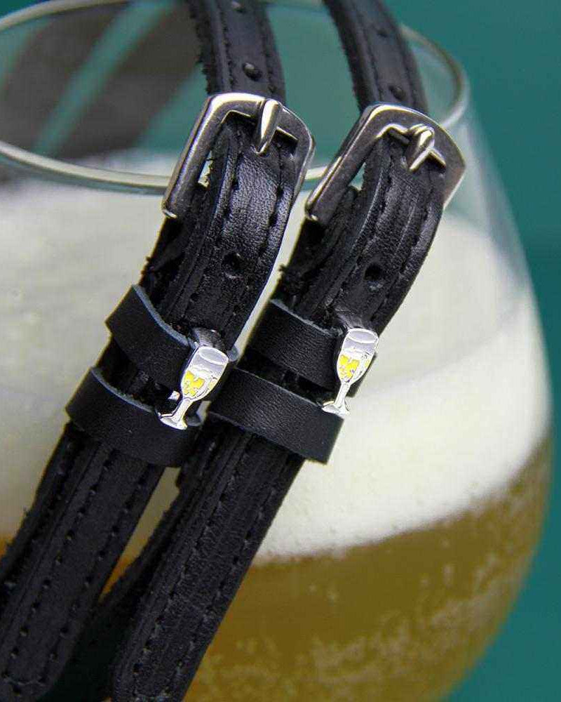 ManeJane champagne spur straps draped over a glass of bubbly on teal