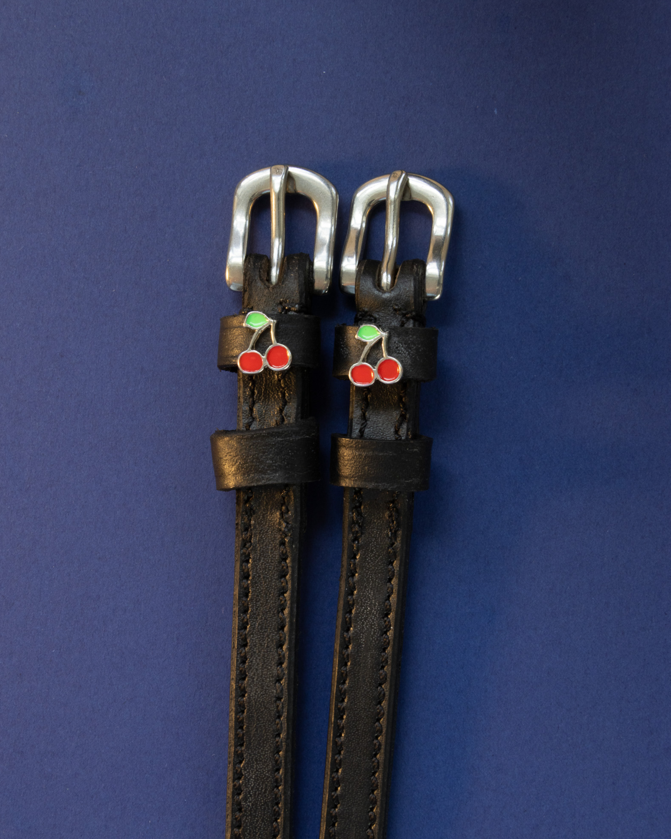 Pair of black leather cherry charm spur straps on a bright yellow background
