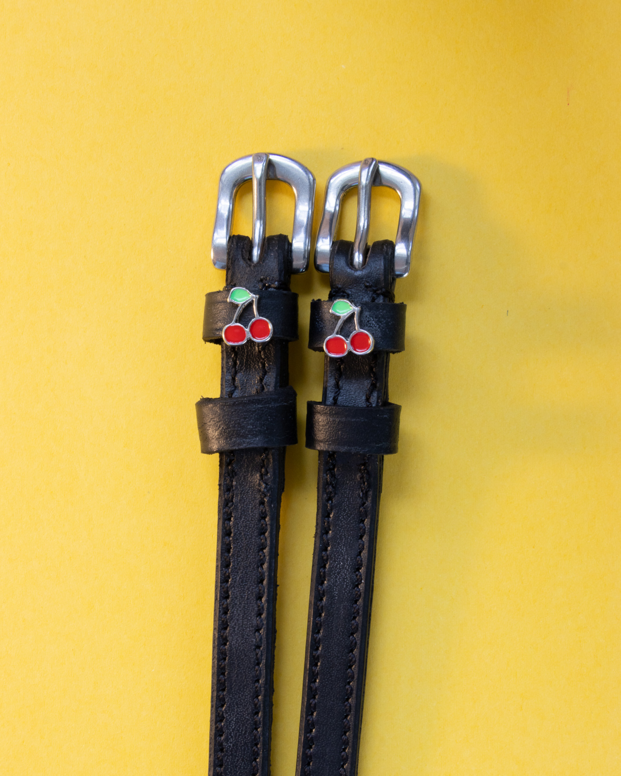 Pair of black leather cherry spur straps with silver buckles on yellow