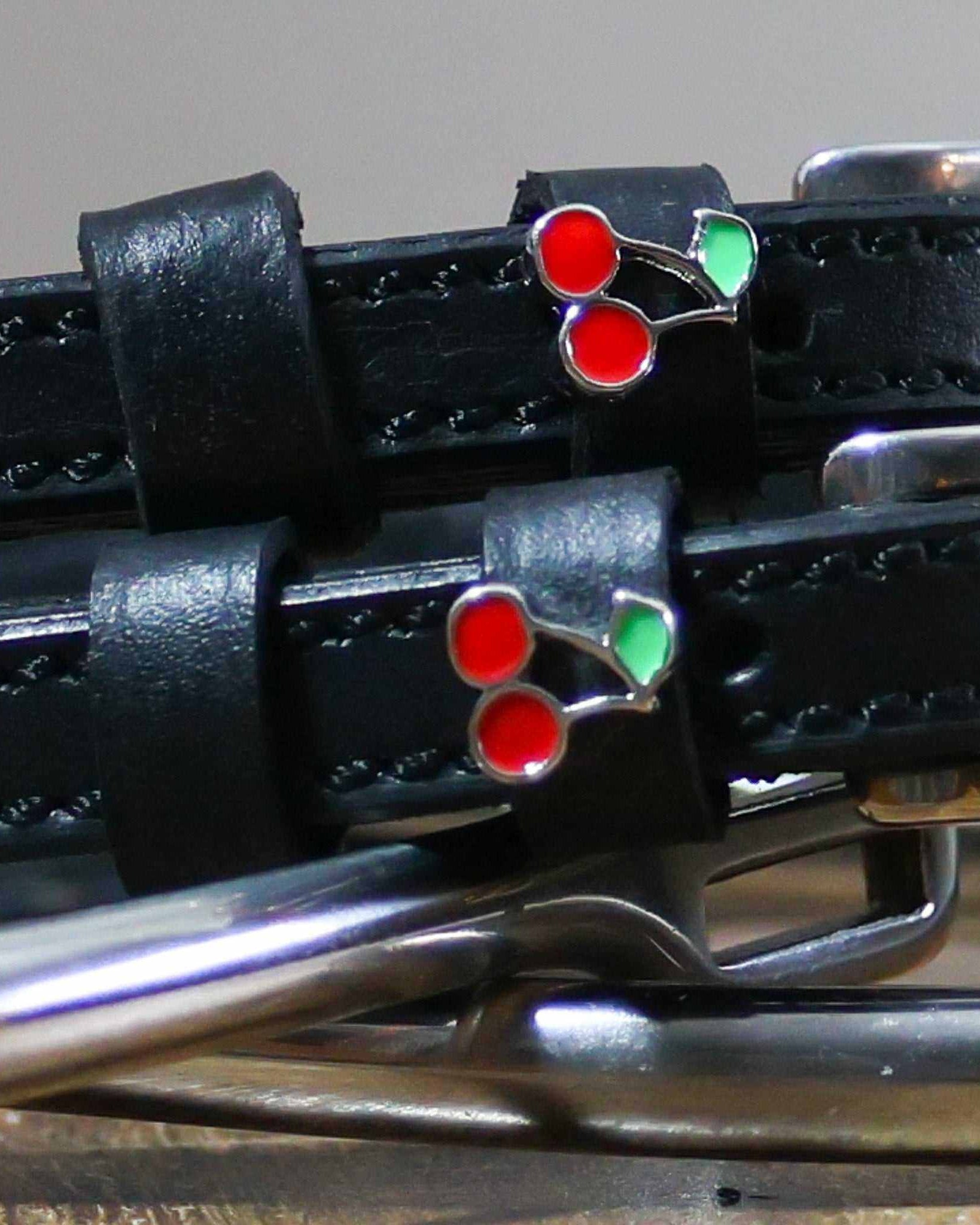 Close-up of a red-and-green enamel cherry charm on a black leather spur strap keeper