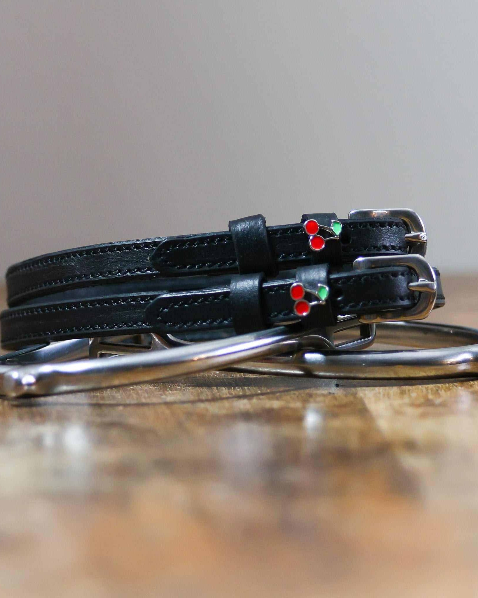 Black leather cherry spur straps coiled beside a metal spur on a wooden surface