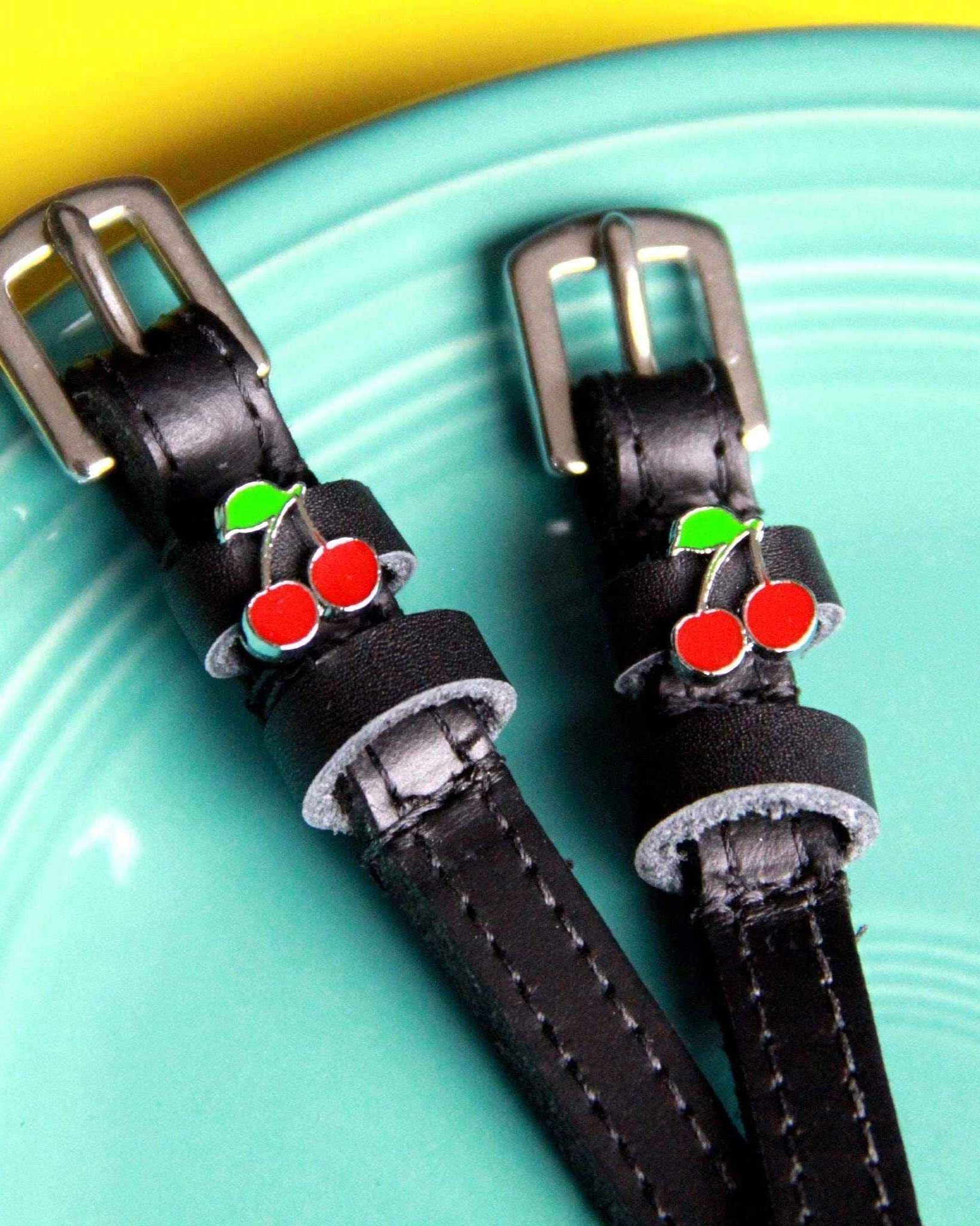 Black leather cherry charm spur straps resting on a teal and yellow dish