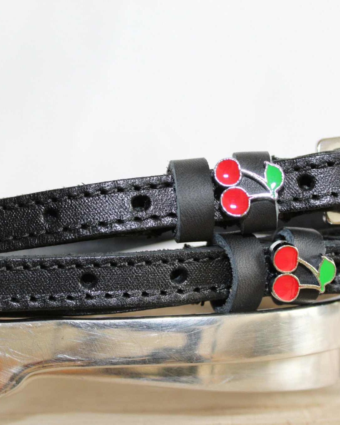 Black leather cherry spur straps laid over a silver spur on a white surface
