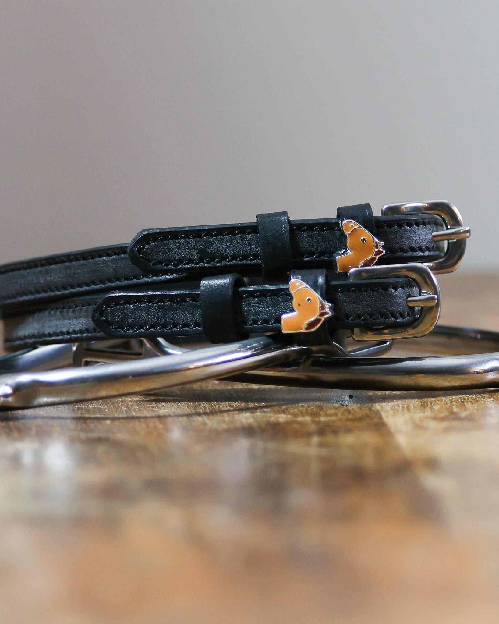 Coiled black leather spur straps and a silver spur on wood with chestnut horse charms