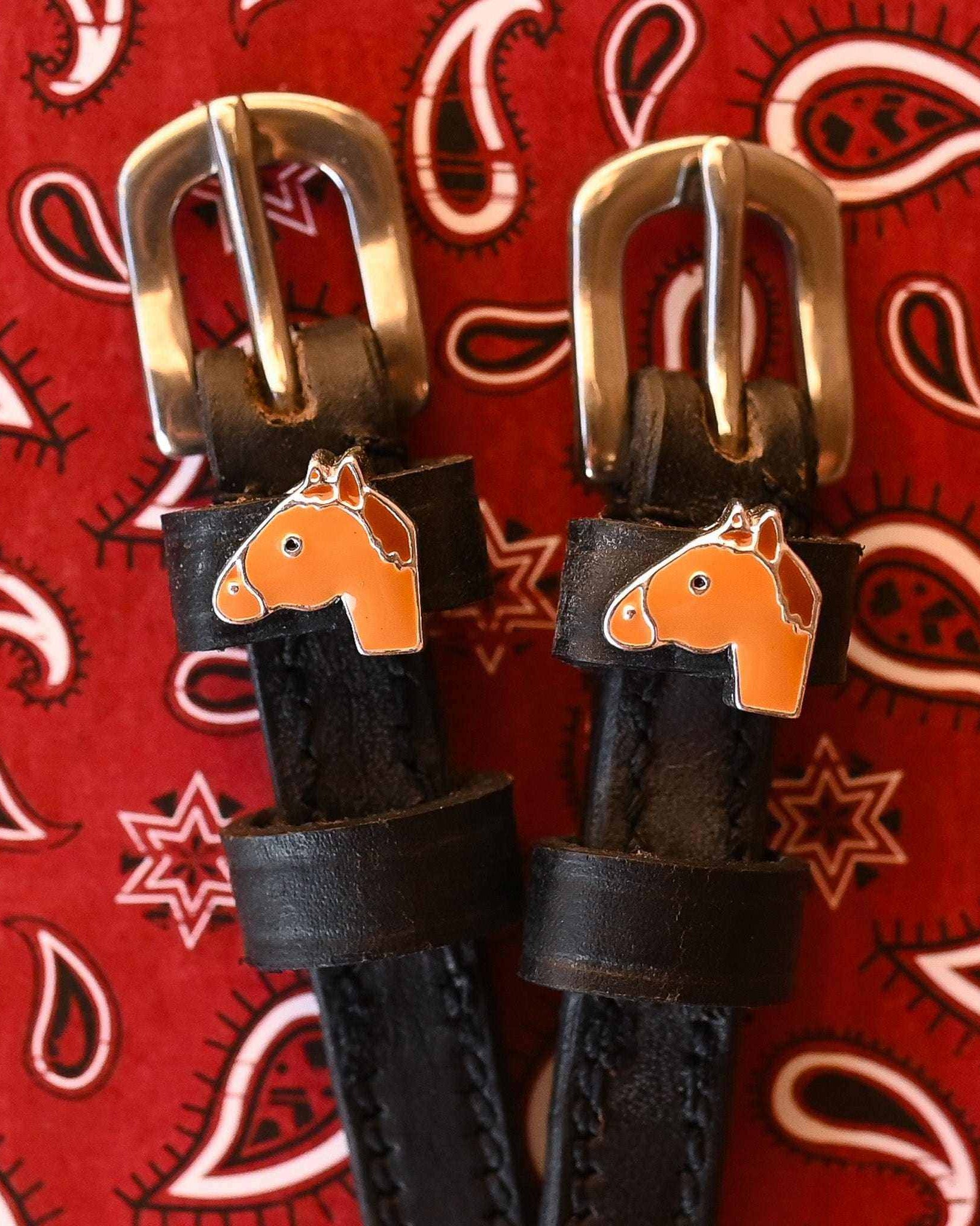Chestnut horse-head charms on black spur straps over a red paisley bandana
