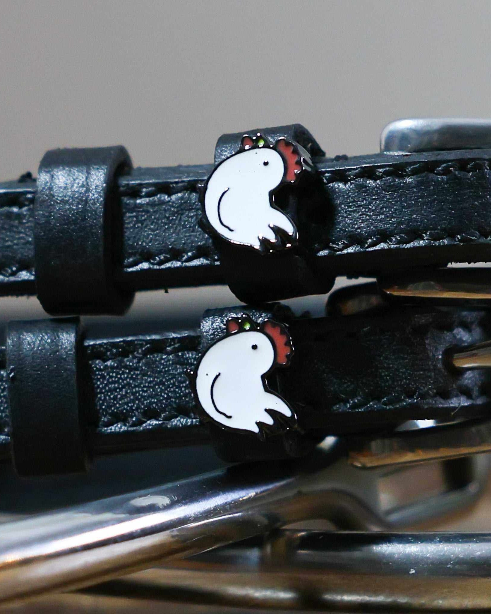 Close-up of white enamel chicken charms on black leather ManeJane spur strap keepers
