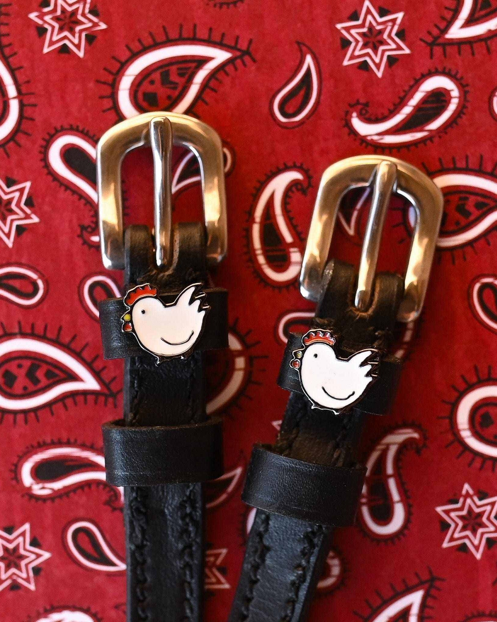 Black leather chicken spur straps with brass buckles on a red paisley bandana background
