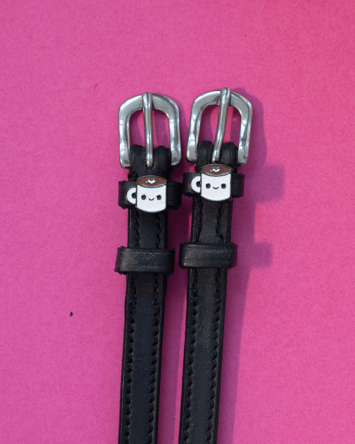 Black leather ManeJane spur straps with smiling coffee-mug charms on pink