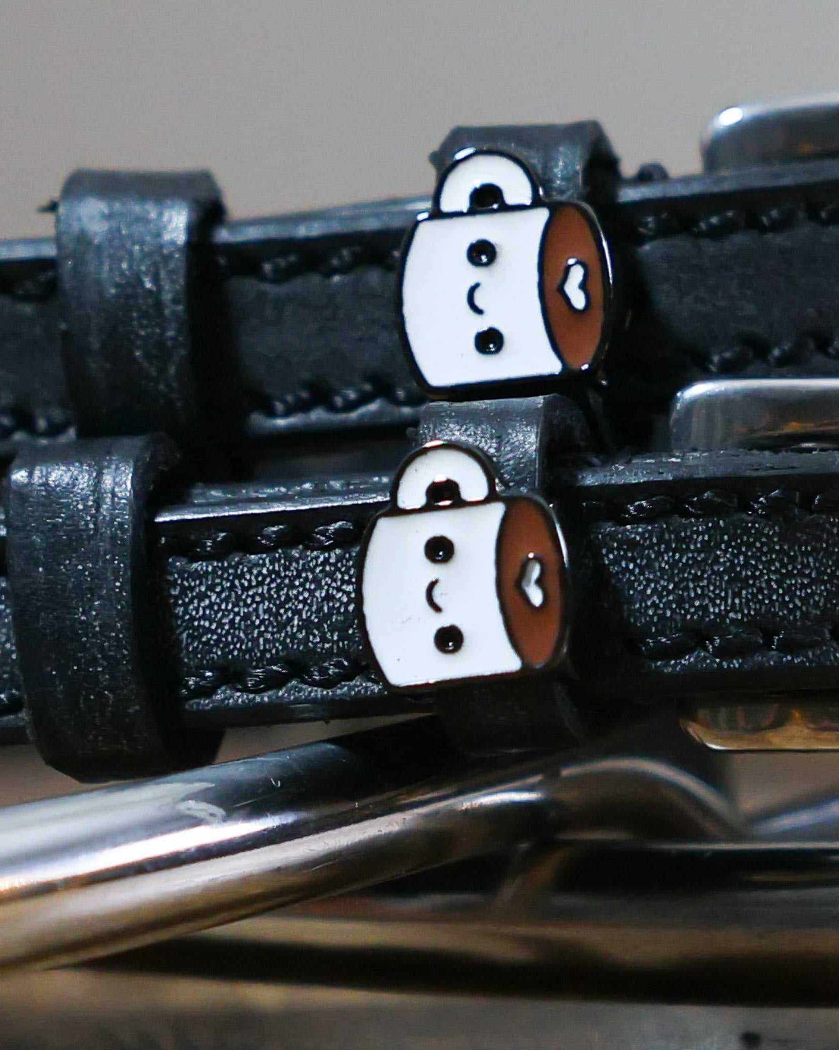 Close-up of kawaii coffee-mug charms on black leather spur strap keepers