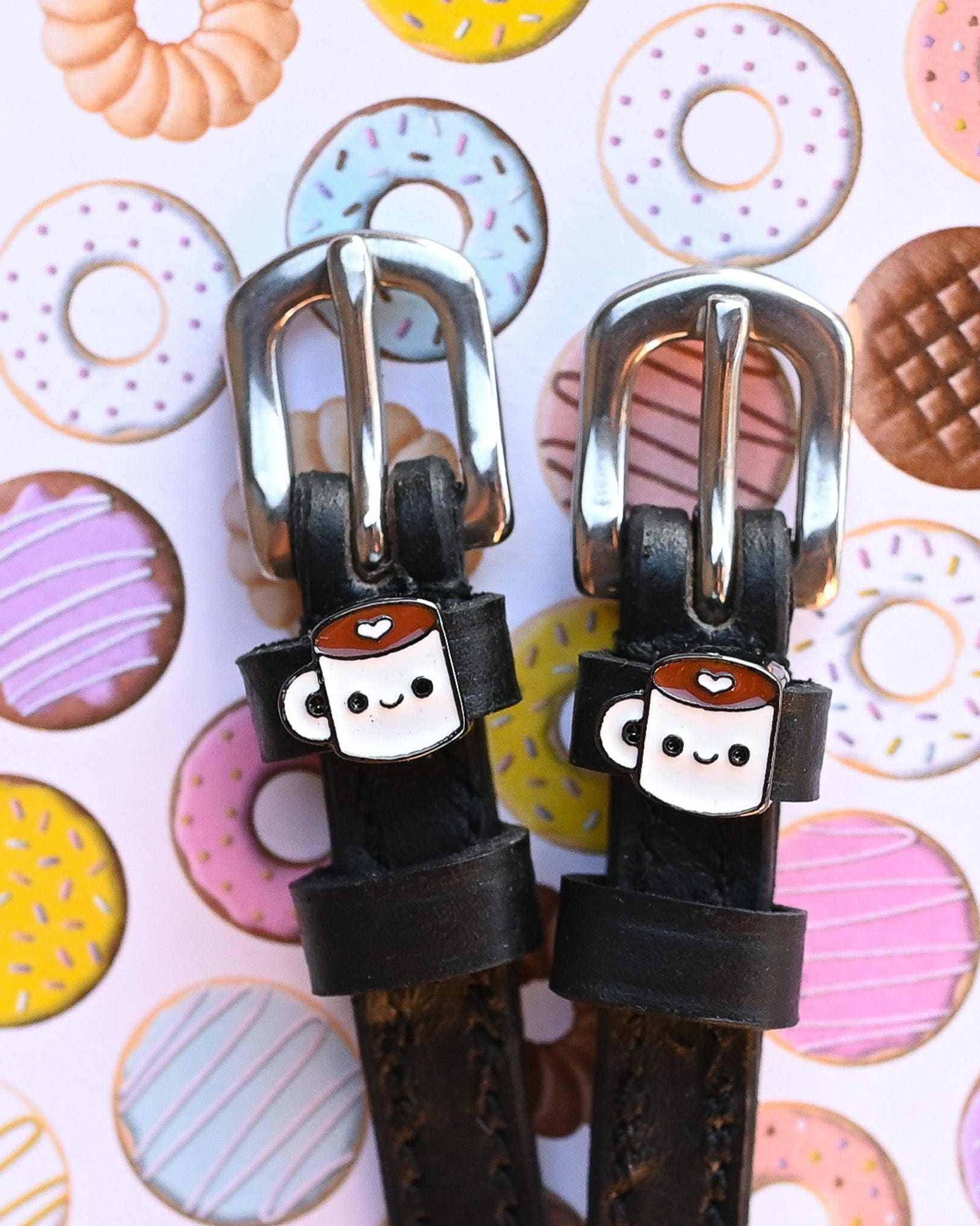 Coffee-mug charm spur straps on a donut-print backdrop, buckle close-up