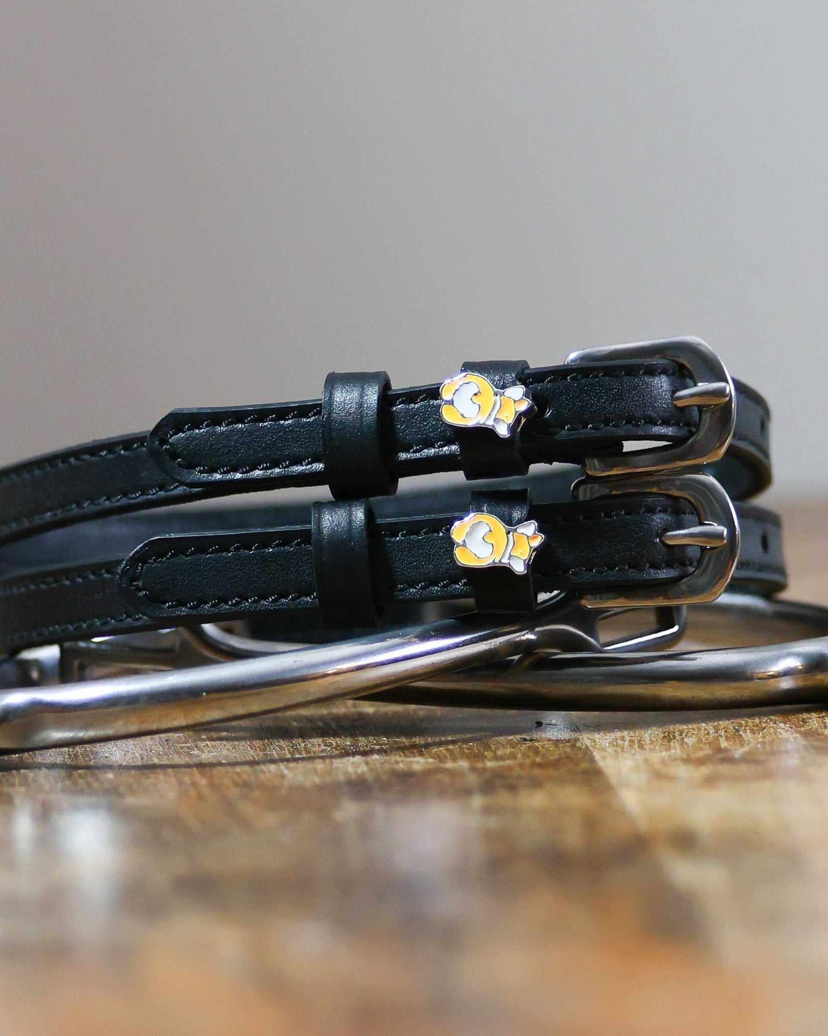 Black leather corgi butt spur straps coiled beside a spur on wood